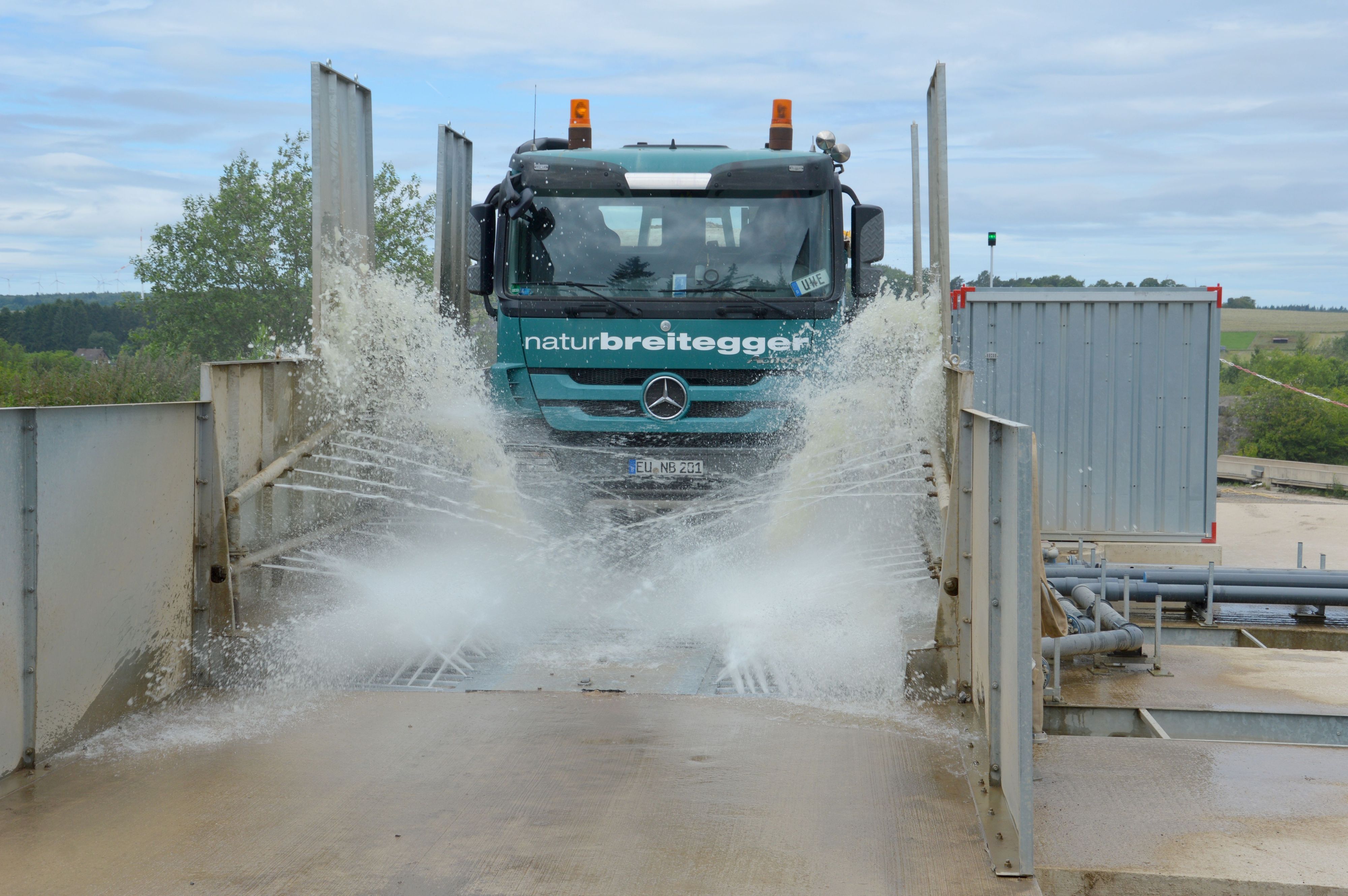 Ein Lastwagen fährt durch die Anlage. Zahlreiche Wasserfontänen sind zu sehen.