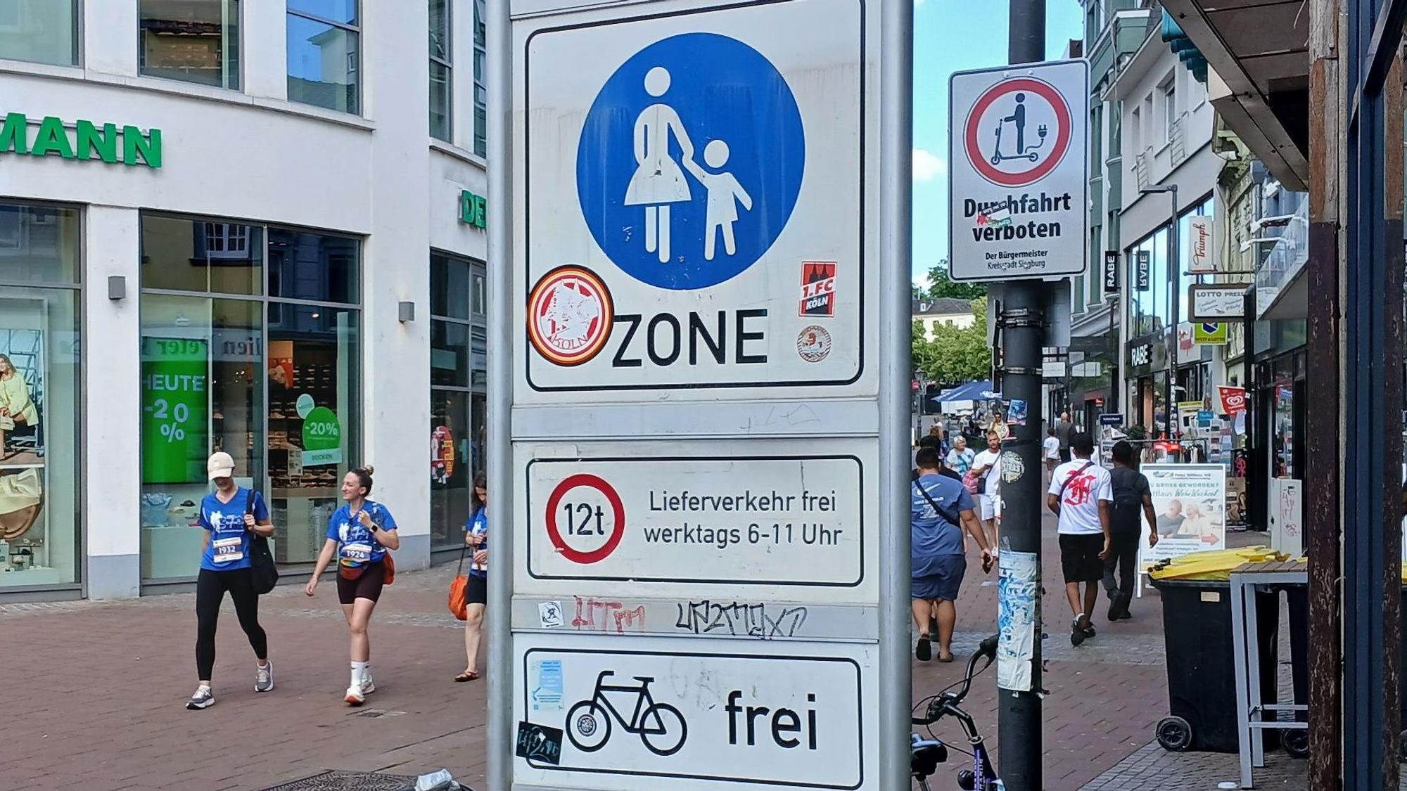 Verkehrsschilder an der Siegburger Fußgängerzone: Die große Tafel verdeckt das Verbot für E-Roller.