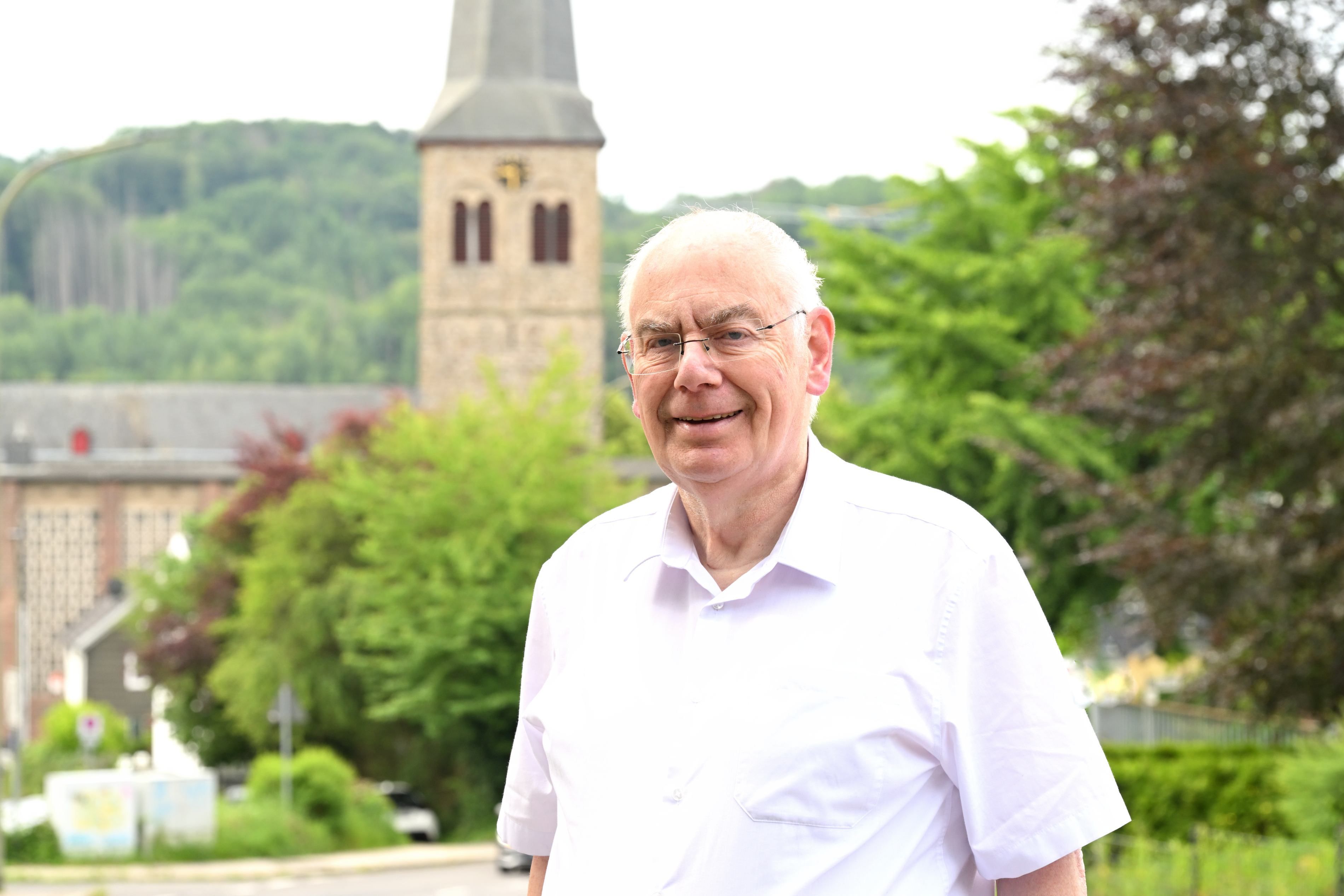 Zu sehen ist ein älterer Mann, der in einiger Entfernung zu einem Kirchturm steht.