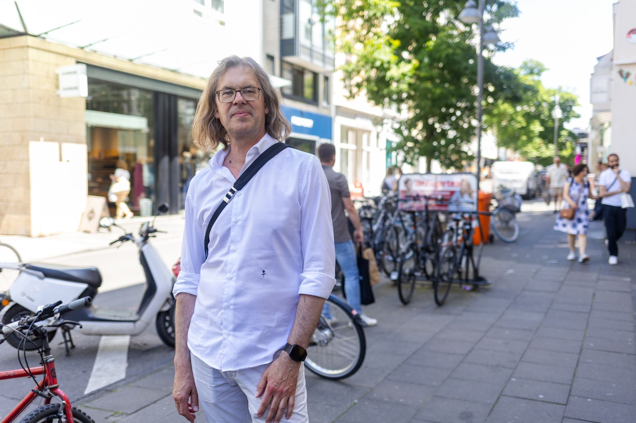 Ein Mann im weißen Hemd und Hose lächelt in die Kamera.