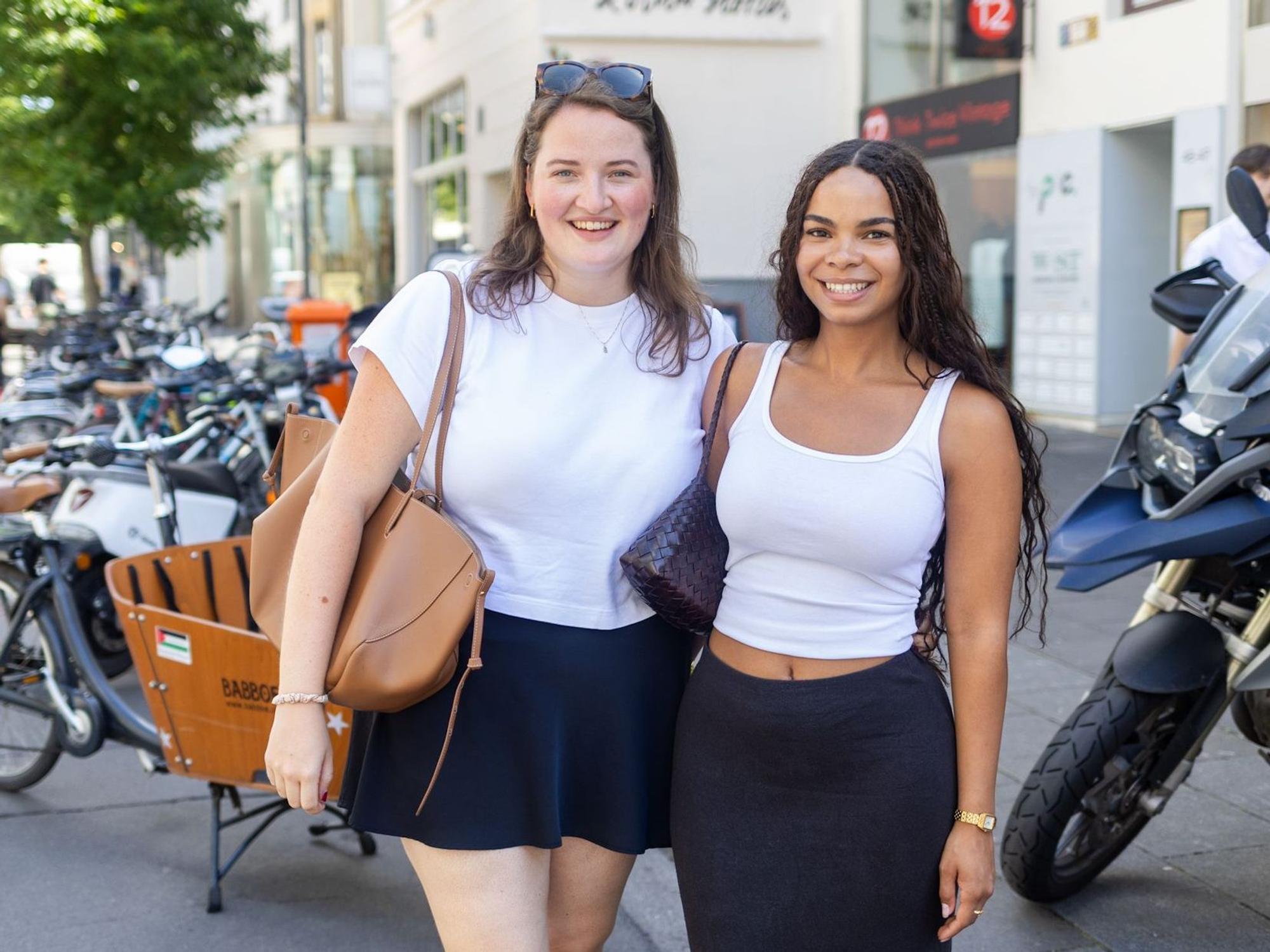 Zwei junge Frauen, sommerlich angezogen, lächeln in die Kamera.