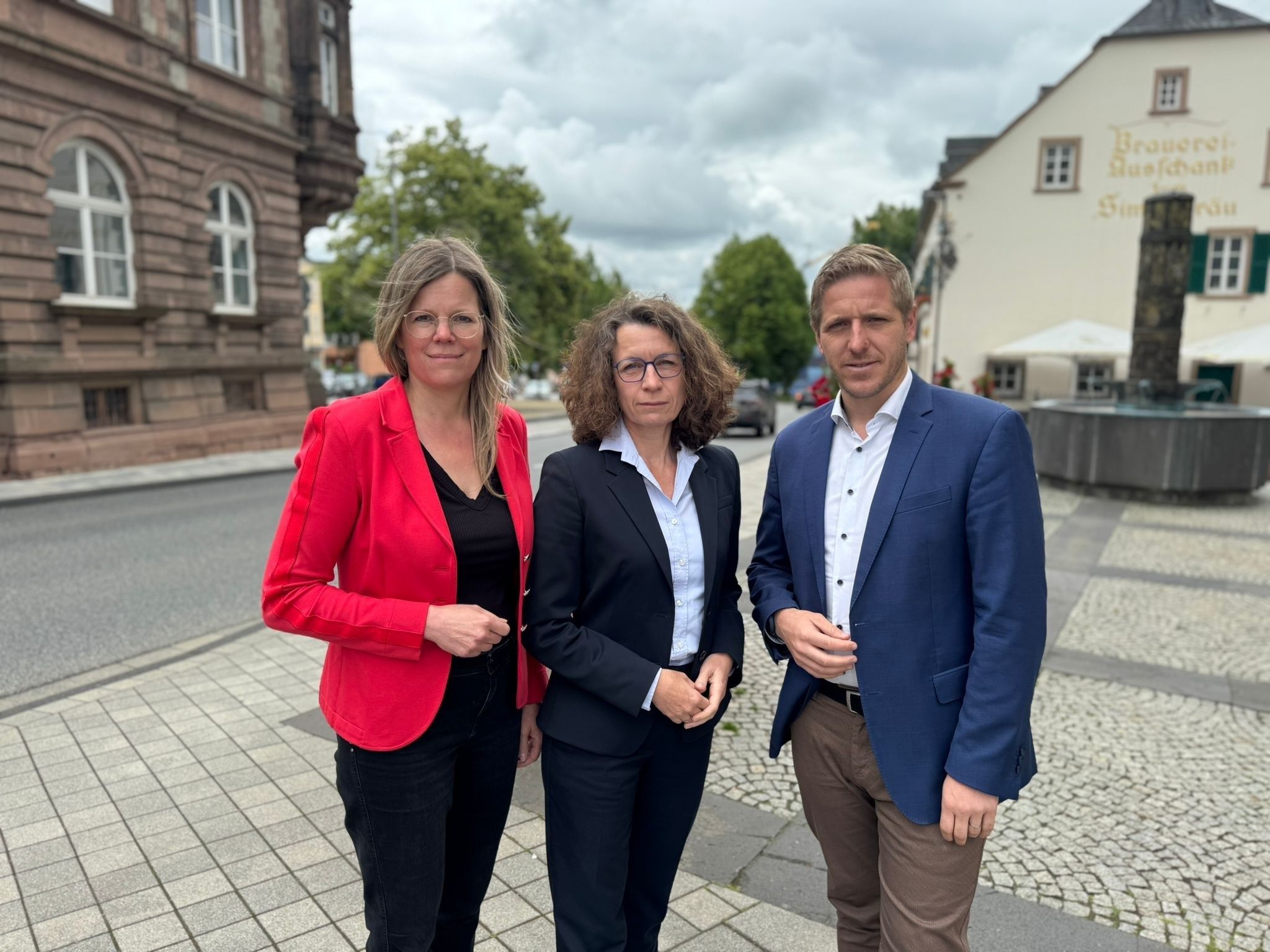 Die drei Obengenannten stehen auf einem gepflasterten Platz.