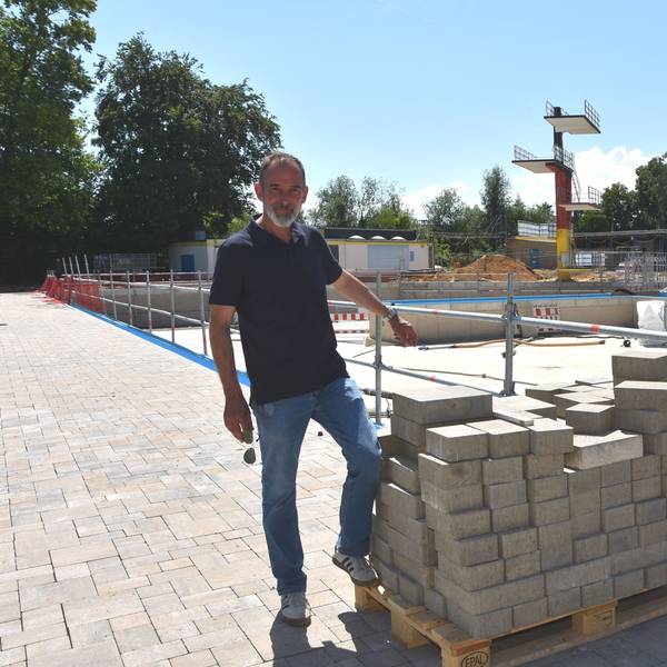 Ein Mann steht vor der Baustelle eines Schwimmbads.