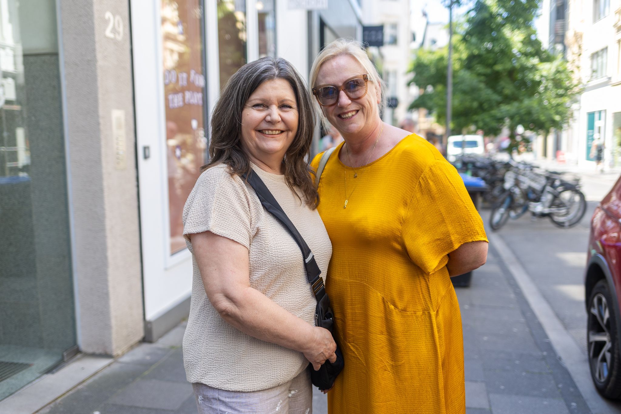 Zwei Frauen im braunen und gelben Kleid lächeln in die Kamera.