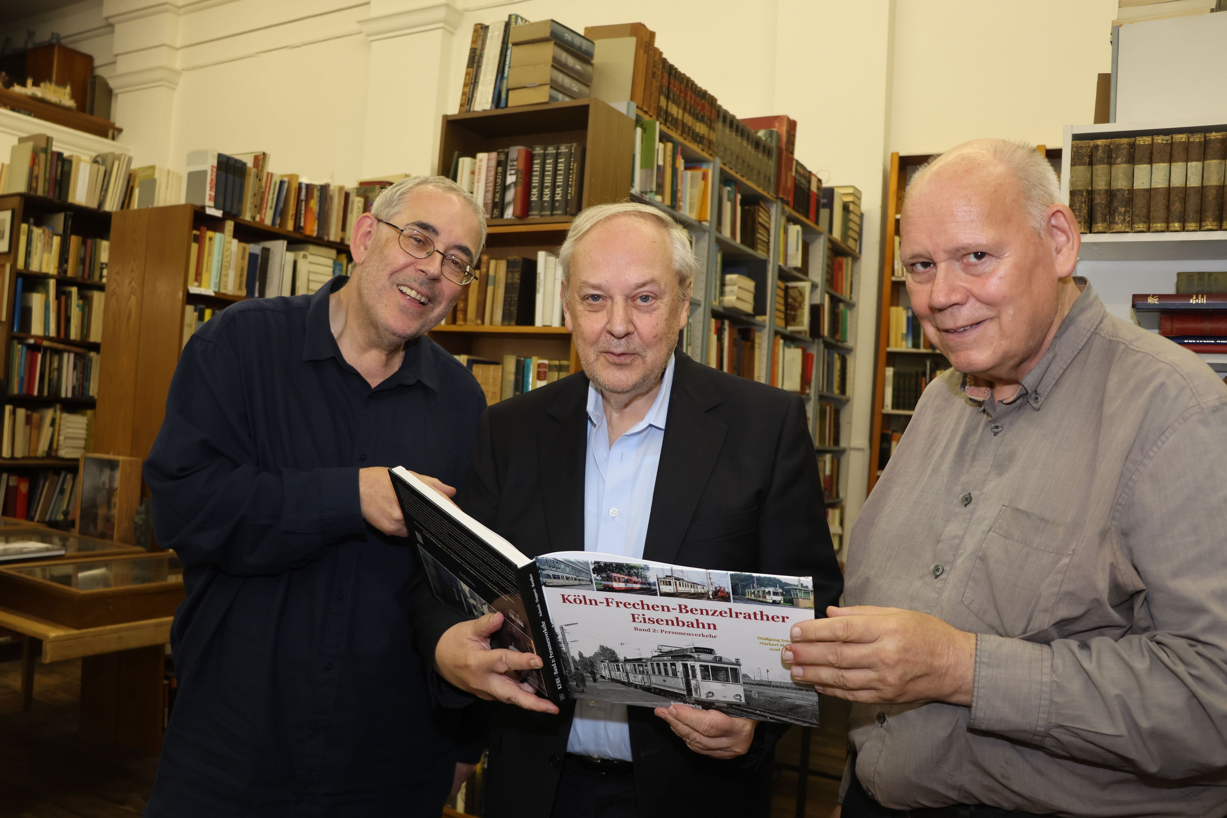 Das Foto zeigt drei Männer die ein Buch in den Händen halten.