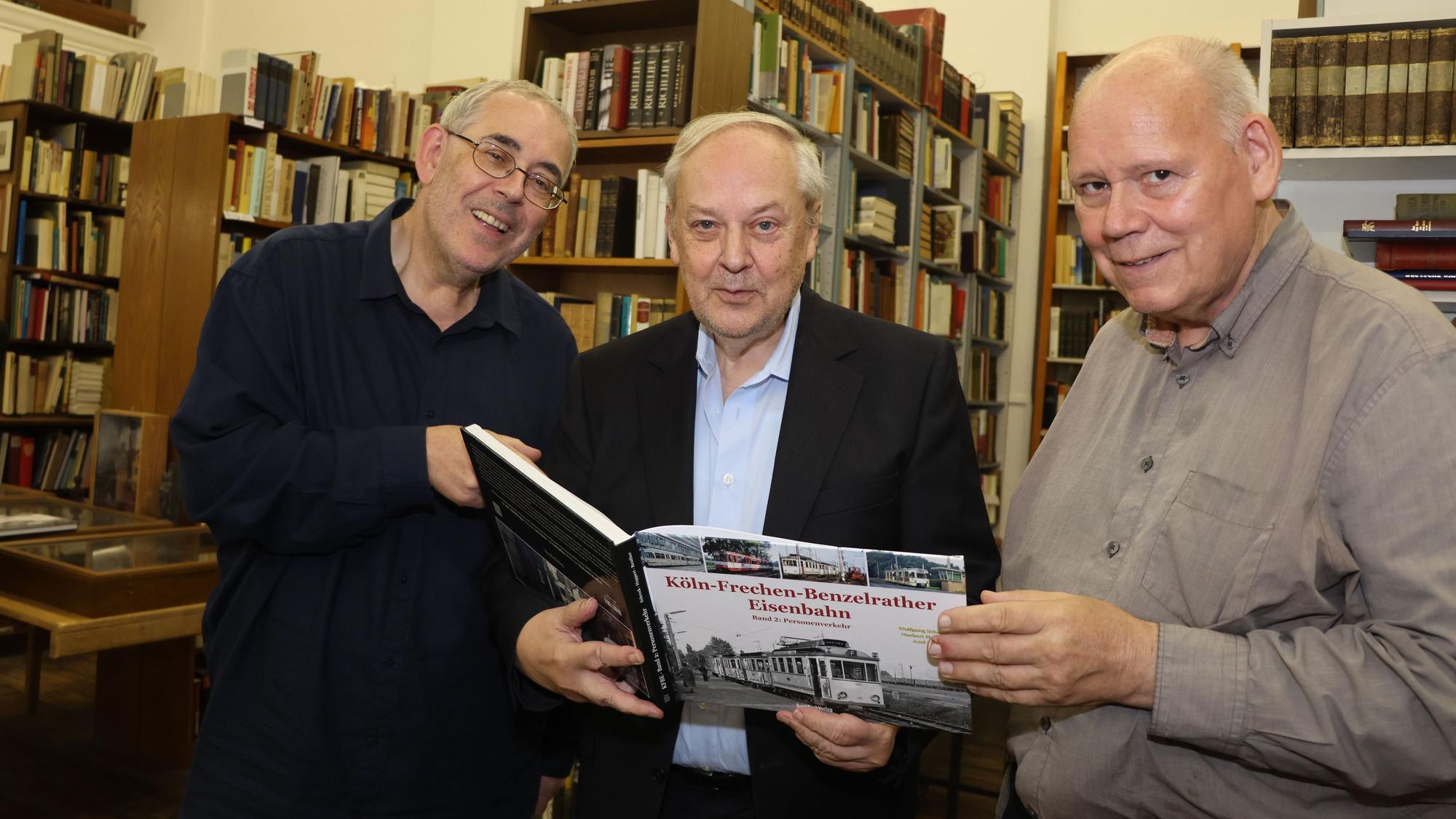 Das Foto zeigt drei Männer die ein Buch in den Händen halten.