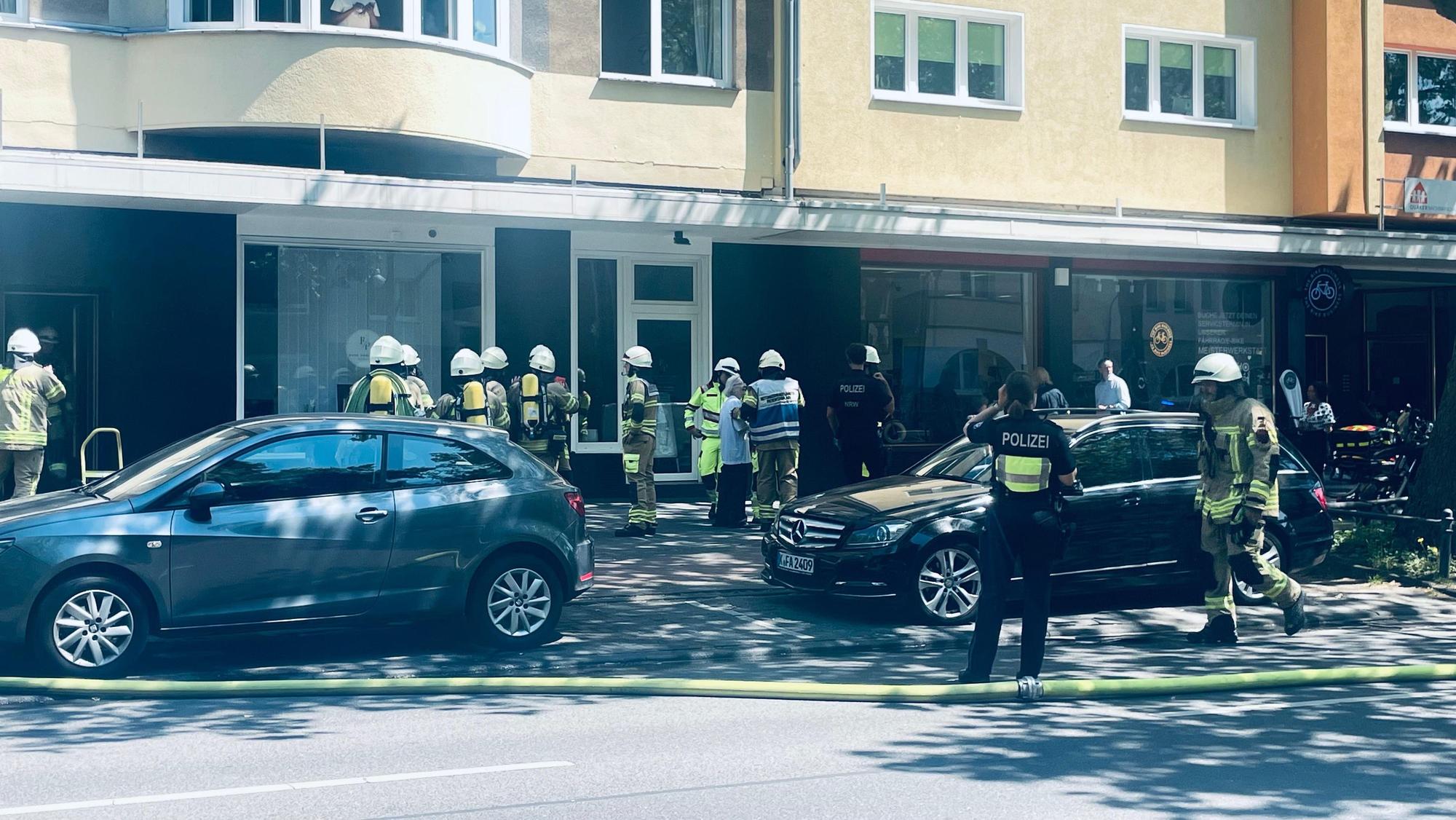 Einsatzkräfte von Feuerwehr und Polizei stehen vor einem Haus, auf der Straße liegt ein Löschschlauch.