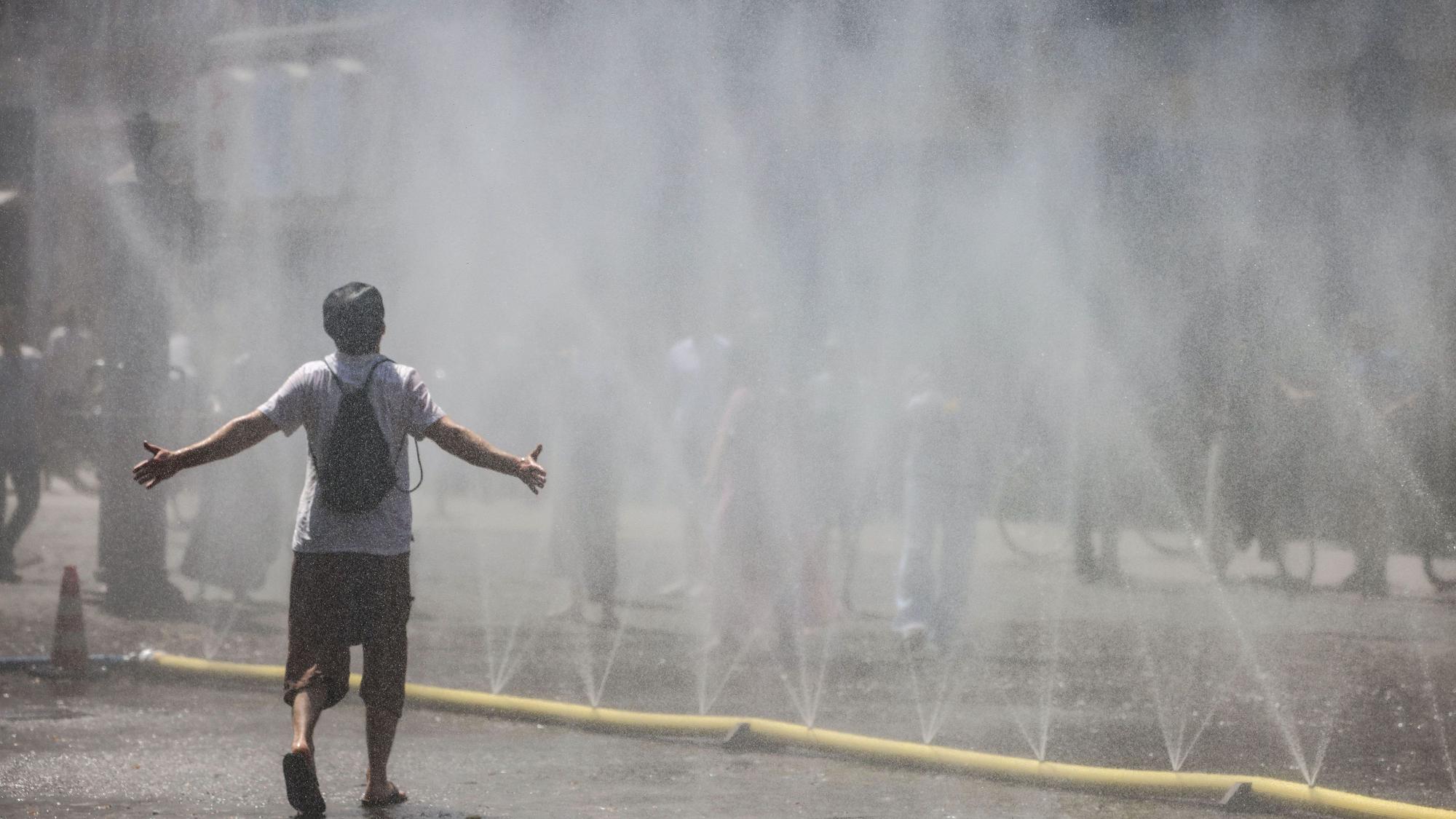 Ein Mann geht an einem Hitzetag durch einen Wassernebel in Köln. (Archivbild)