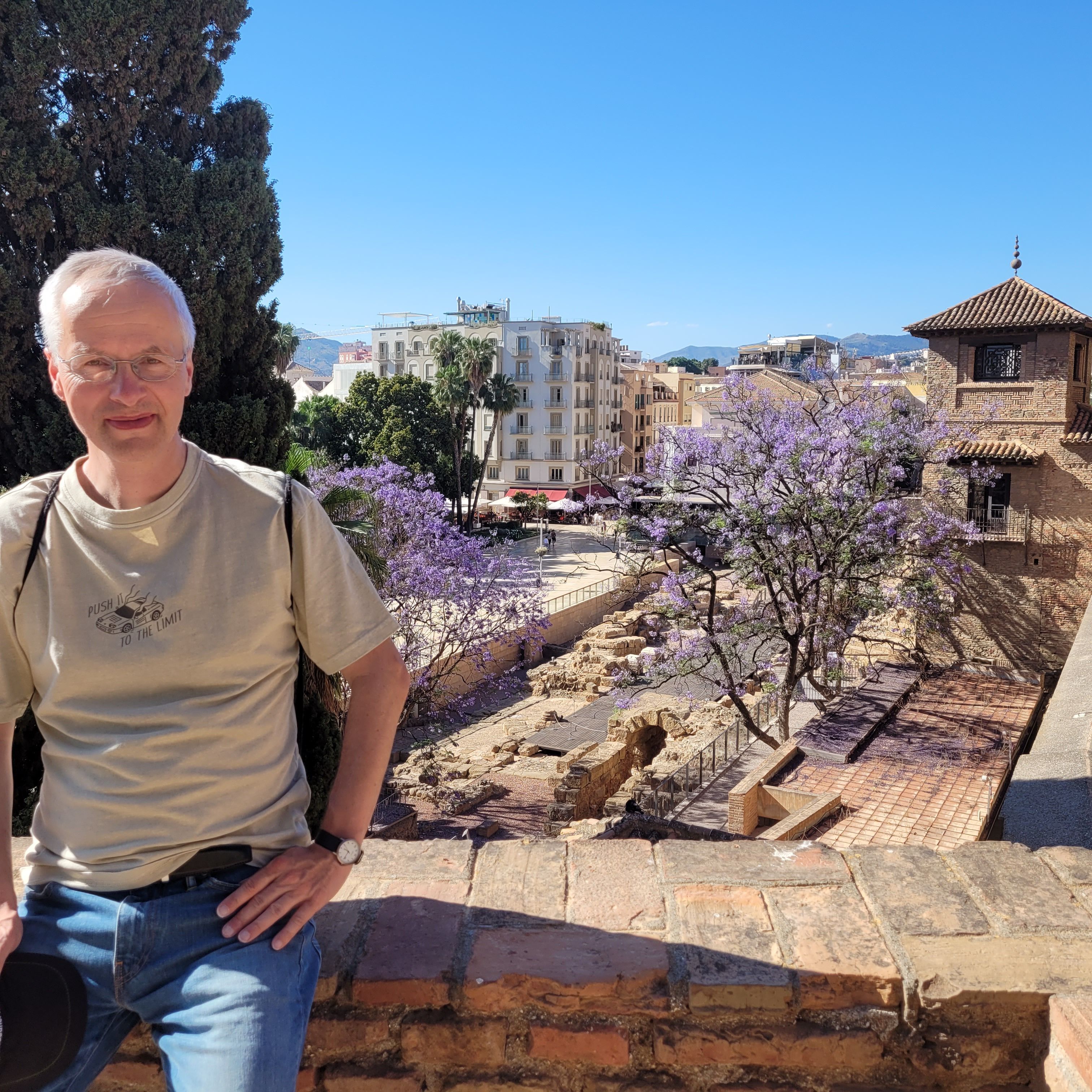 Zu sehen ist ein Mann in einer mediterranen Stadt, der in die Kamera lächelt.