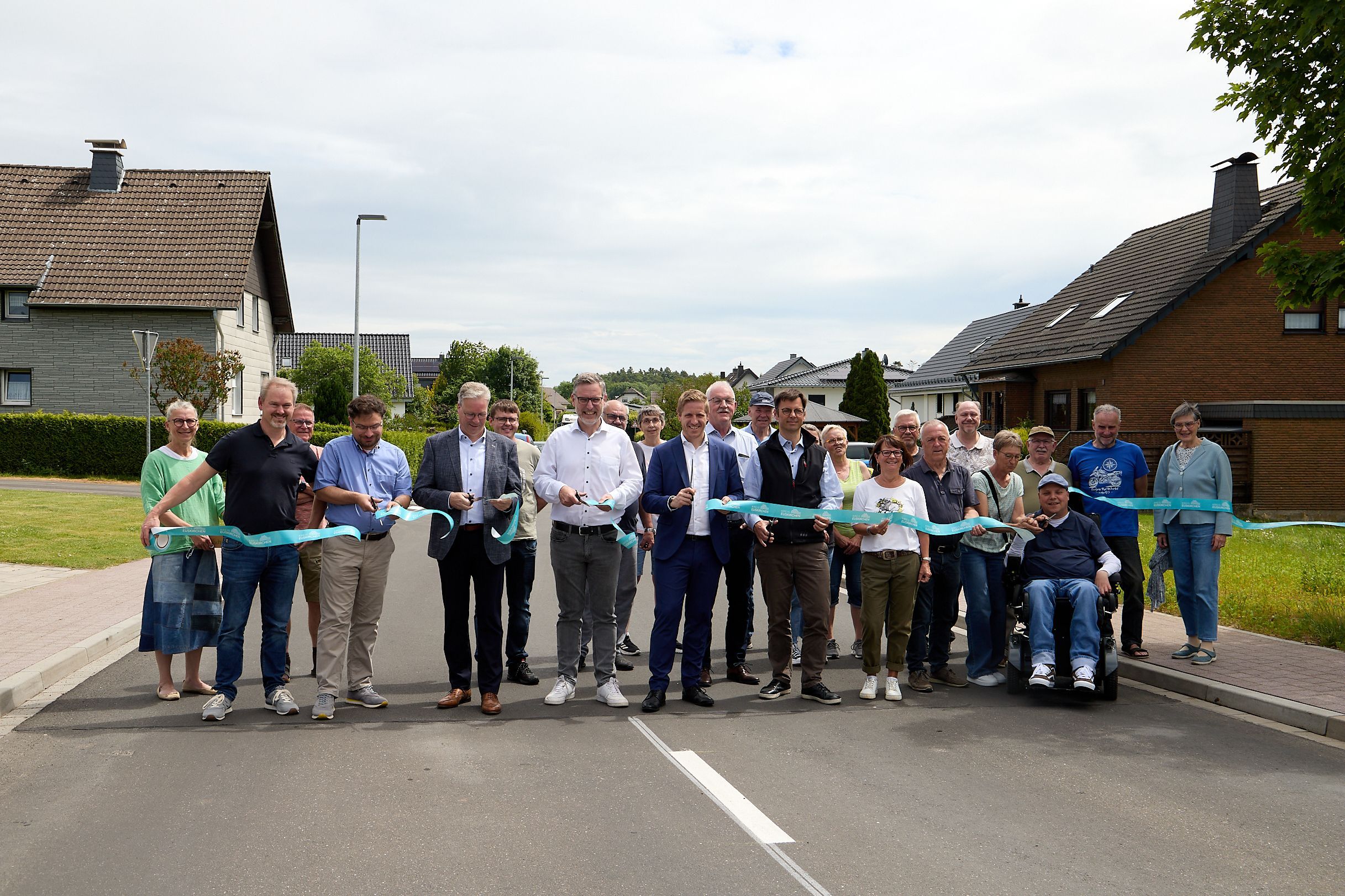 Eine Gruppe Menschen steht auf der Straße. Sie durchschneiden an meheren Stellen ein blaues Band.