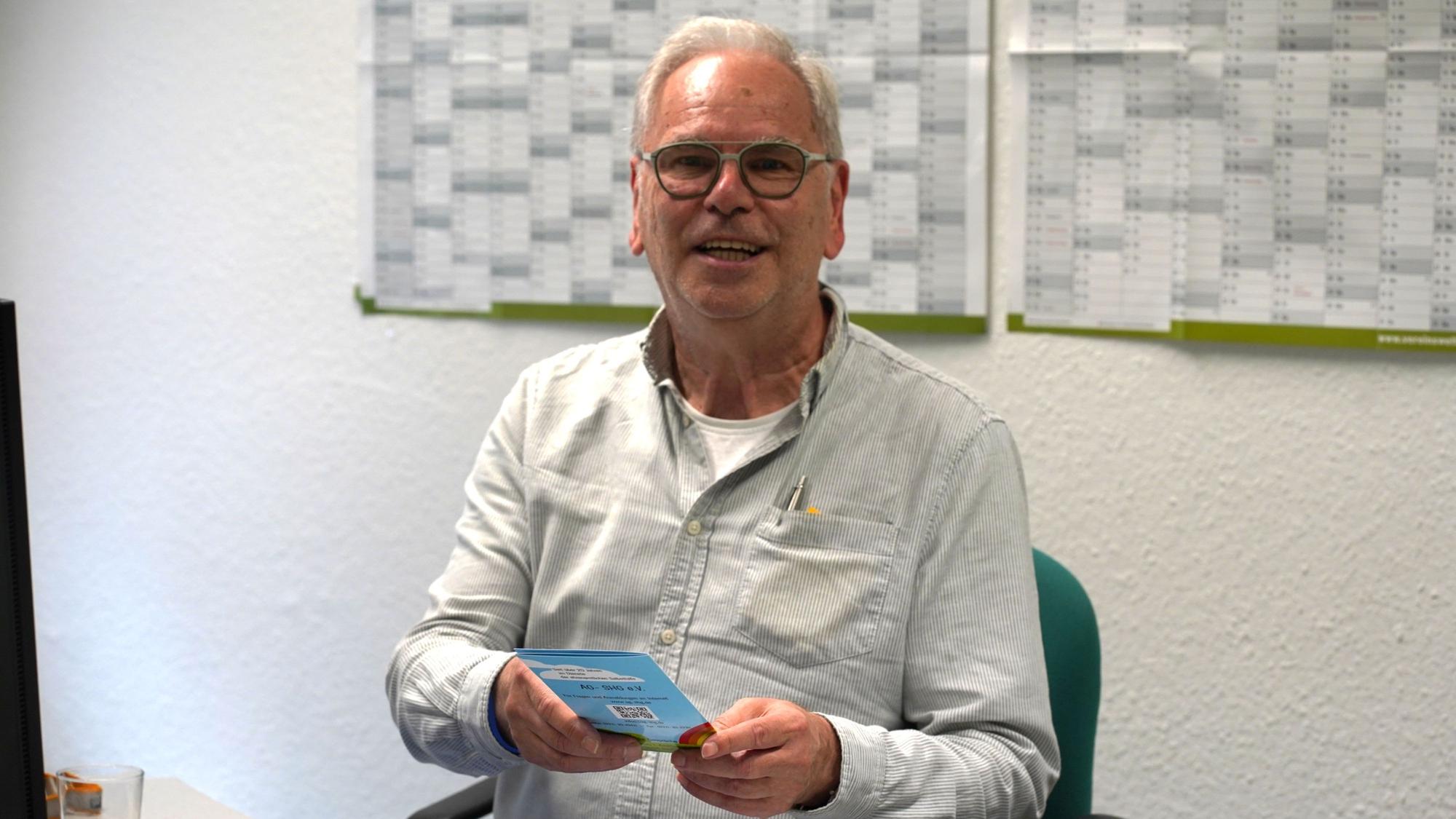 Das Foto zeigt einen Mann mit einer Broschüre in der Hand.