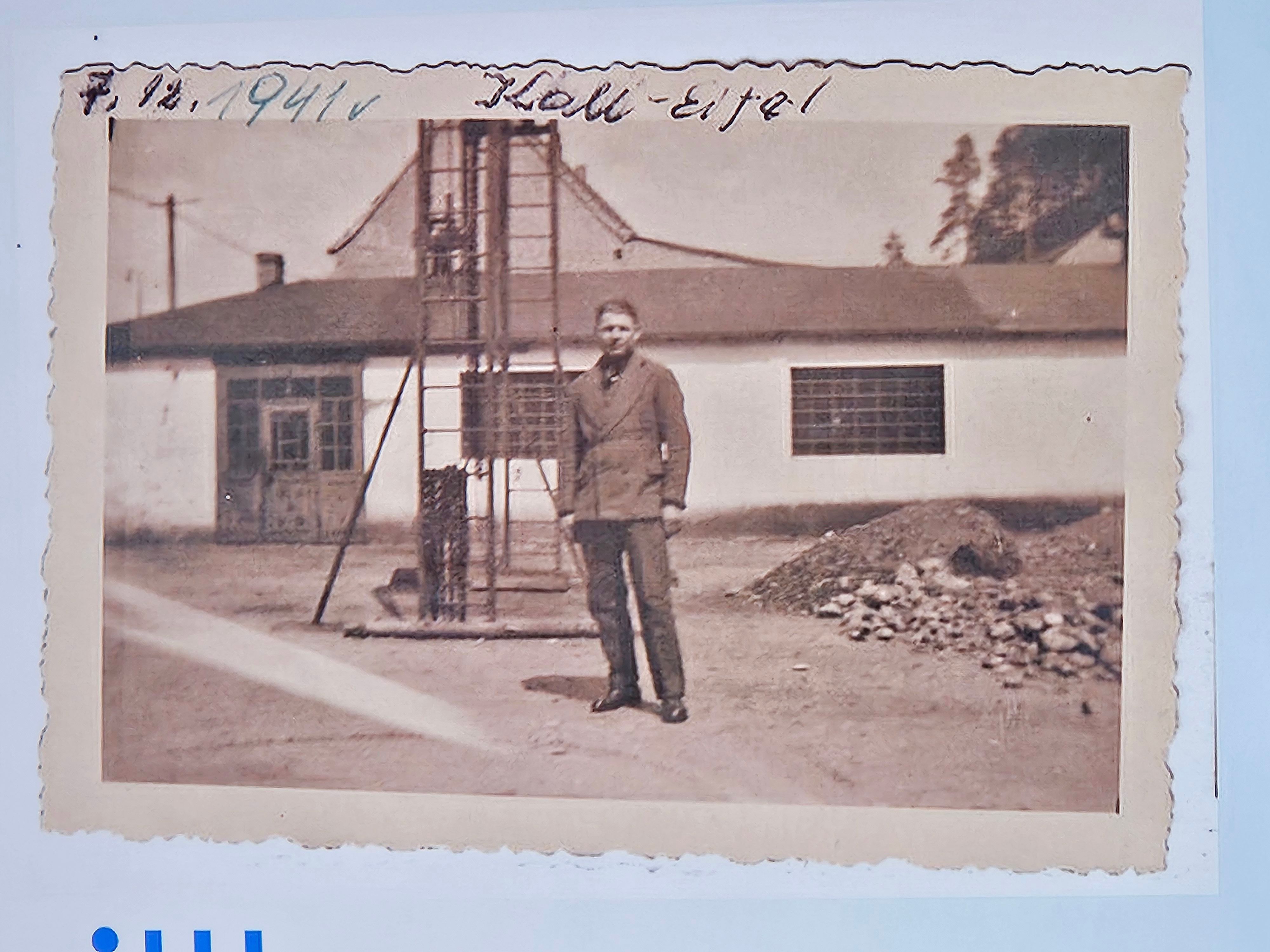 Das Bild ist ein schwarz-weiß Foto. Ein Mann steht vor einer Halle.