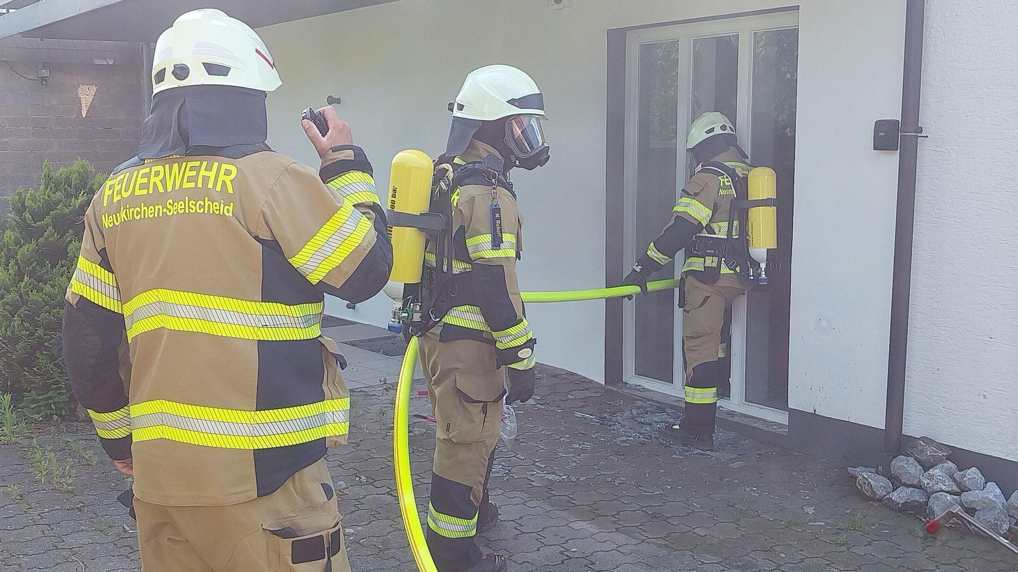 Drei Feuerwehrleute stehen mit einem Löschschlauch vor dem Erdgeschoss eines Hauses.