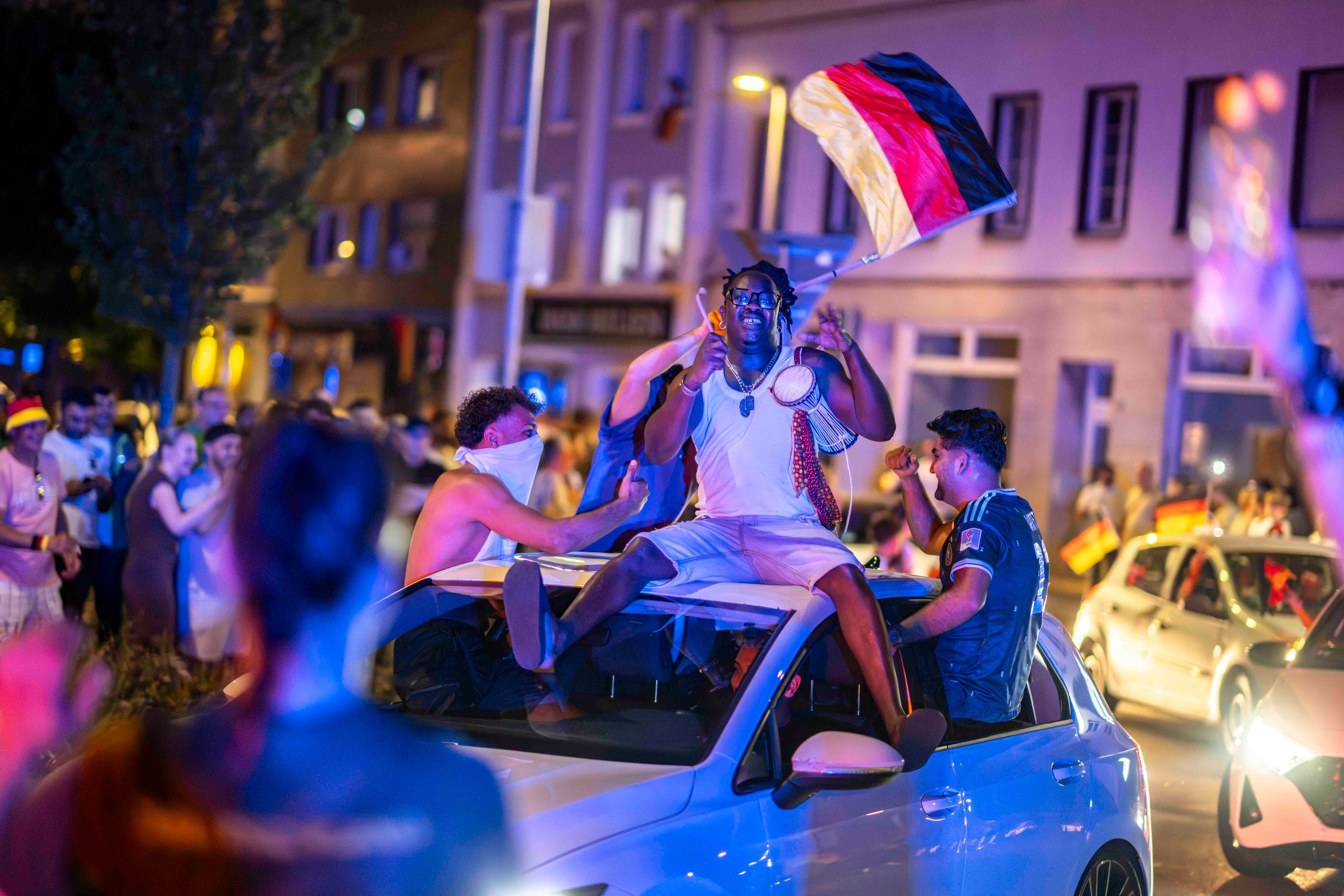 Autos drehen ihre Runde durch den Kreis-Verkehr. Auf dem Dach eines Wagens sitzt ein Mann mit einer kleinen Trommel. Ein anderer wedelt mit den Deutschland-Fahne.