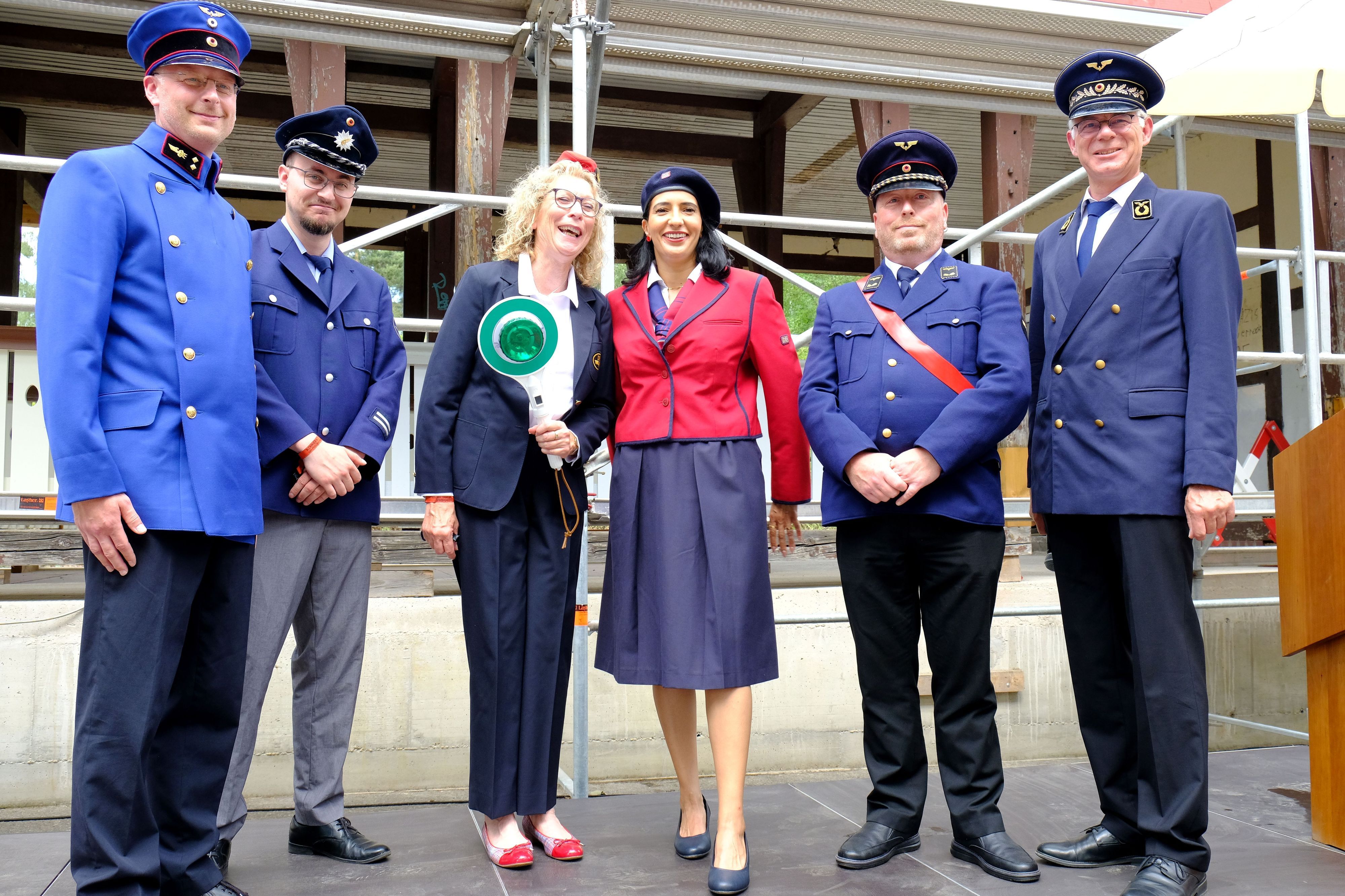 Vier Männer und zwei Frauen stehen in Bahnuniformen aus verschiedenen Epochen vor dem Bahnhofsgebäude aus Walporzheim.