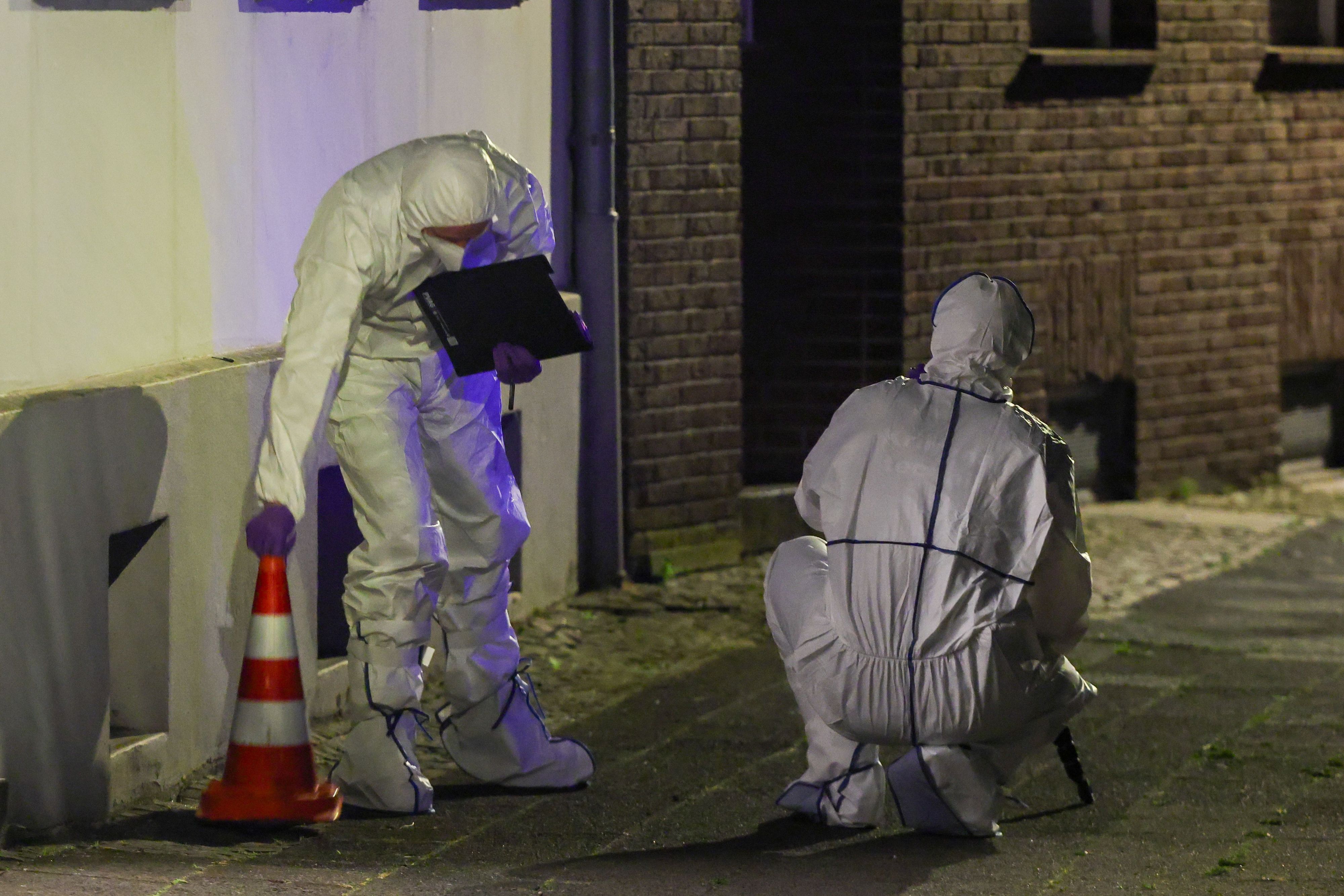 Zwei Beamte der Spurensicherung in Spurensicherungsanzügen begutachten den Tatort vor einem Mehrfamilienhaus im Stadtteil Uerdingen.