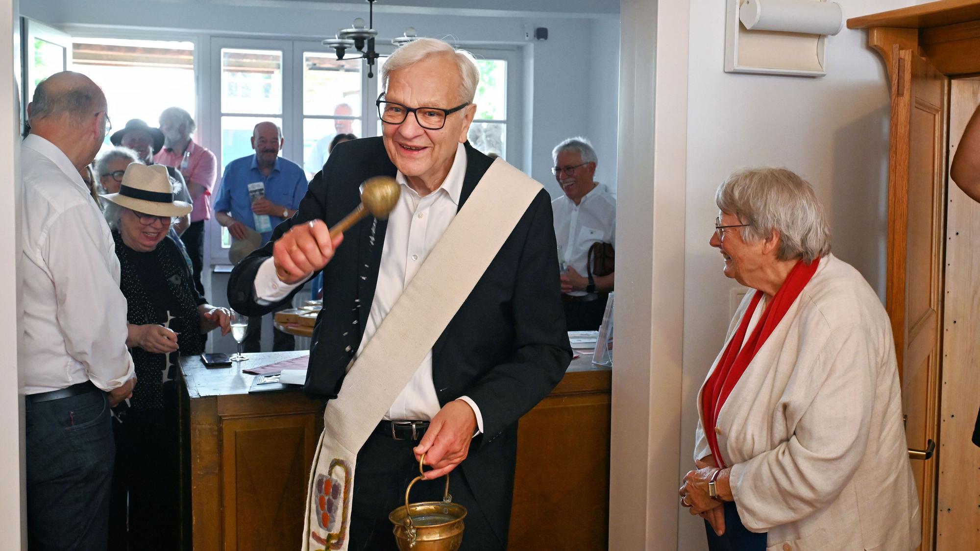 Diakon Ulrich Günzel bei der Einsegnung mit Weihwasserbehälter und Aspergill. Neben ihm steht eine Frau mit einer weißen Jacke.
