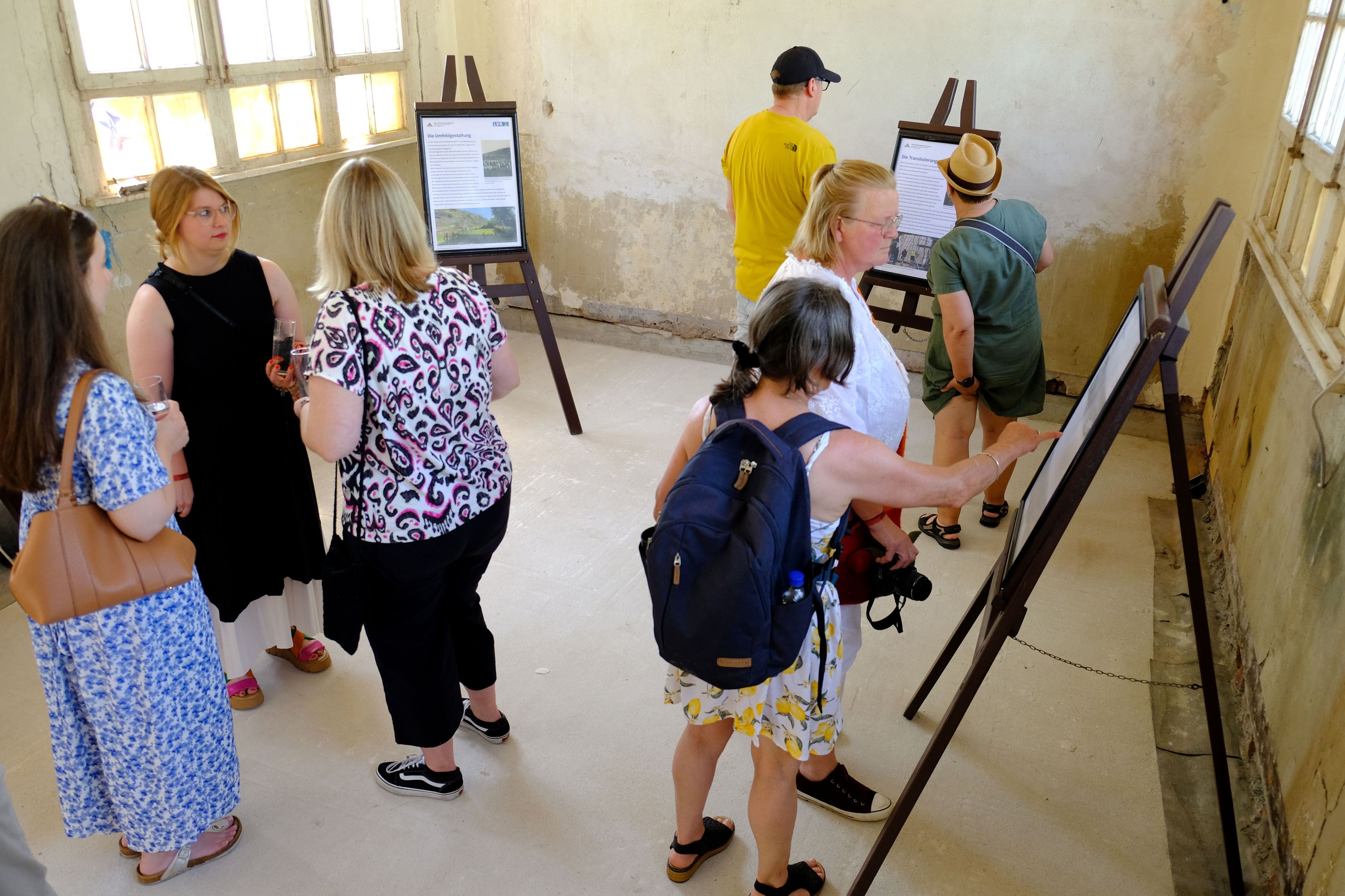 Mehrere Besucher halten sich im Wartesaal des Bahnhofs auf, der sich noch im Rohzustand befindet und in dem mehrere Infotafeln aufgebaut sind.