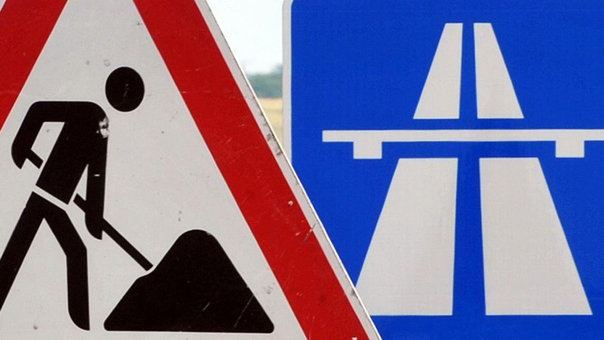 Ein Baustellenschild ist vor einem Autobahnschild platziert.
