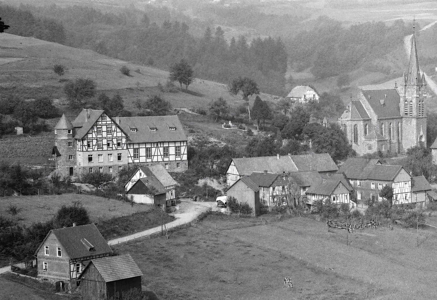 Dieses historische Foto aus Morsbach zeigt das Gesellenhaus in Holpe (links) in den 1930er Jahren. Vor 100 Jahren wurde der Grundstein gelegt, was am 28. Juni 2026 in der Kirche St. Mariä Heimsuchung (rechts) mit einem Gottesdienst gefeiert wird.