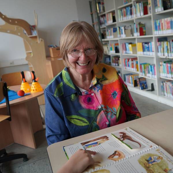 Das Bild zeigt die Seniorin im Lesewald der Rochusschule in Glessen. Vor ihr zeigt ein Kind gerade auf ein Buch.