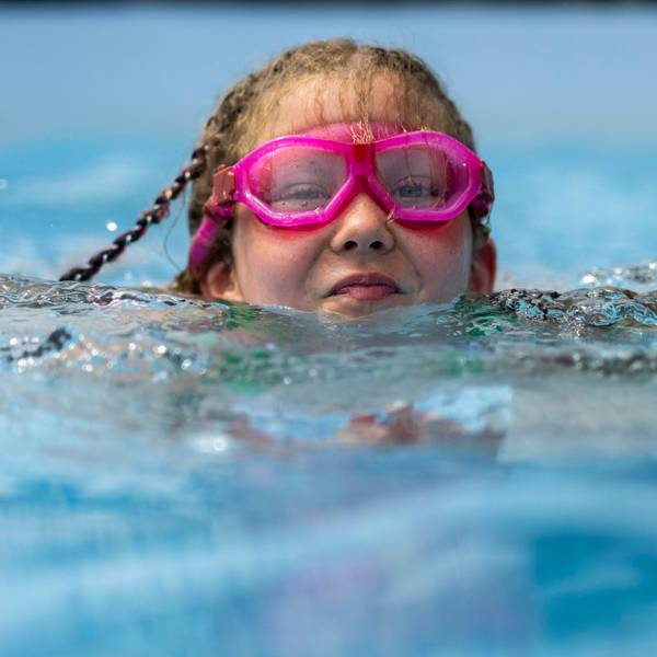 Ein Kind mit rosa Brille schwimmt im Wasser.