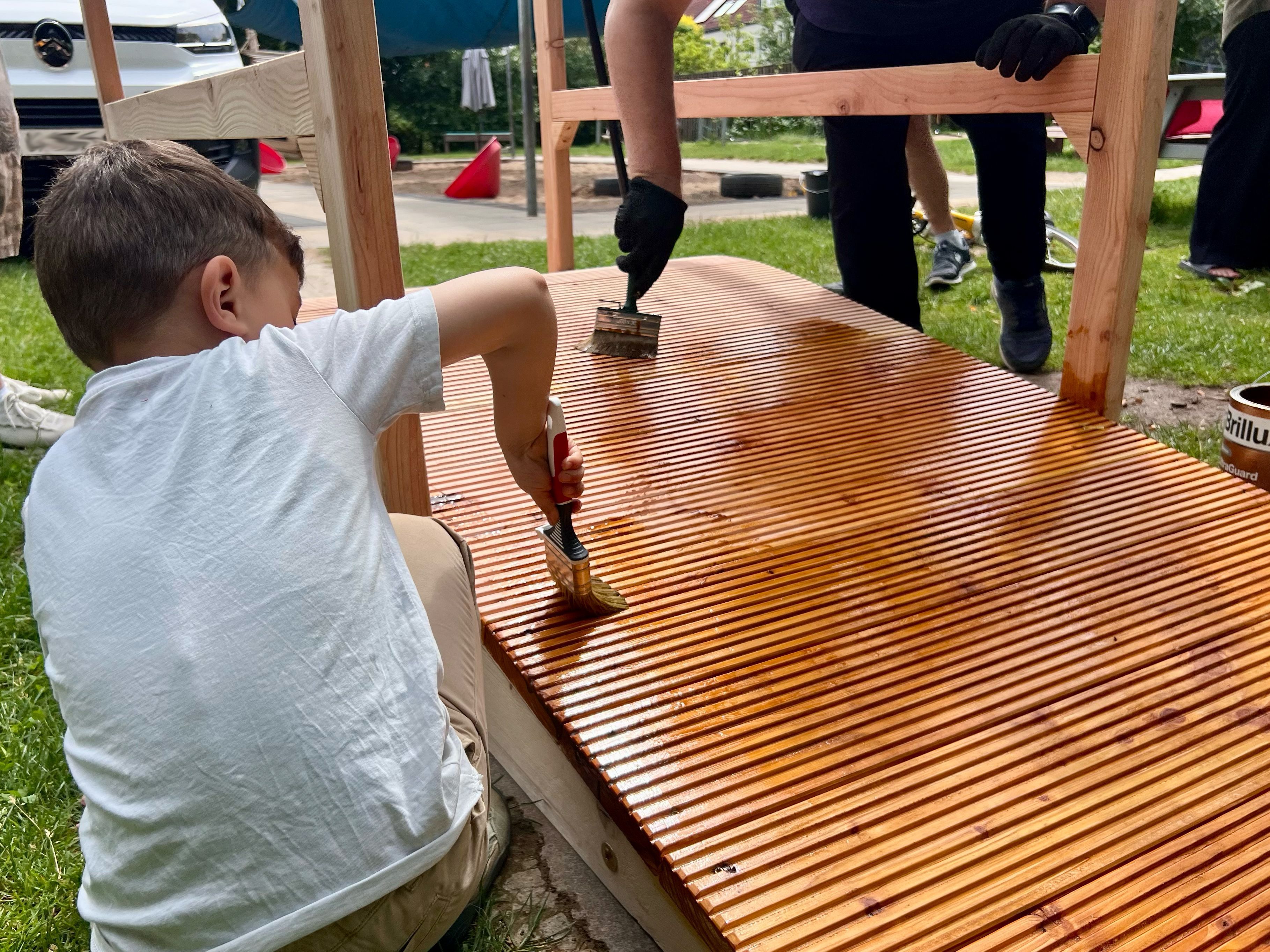 Ein Junge lackiert eine Holzfläche mit einem breiten Pinsel.