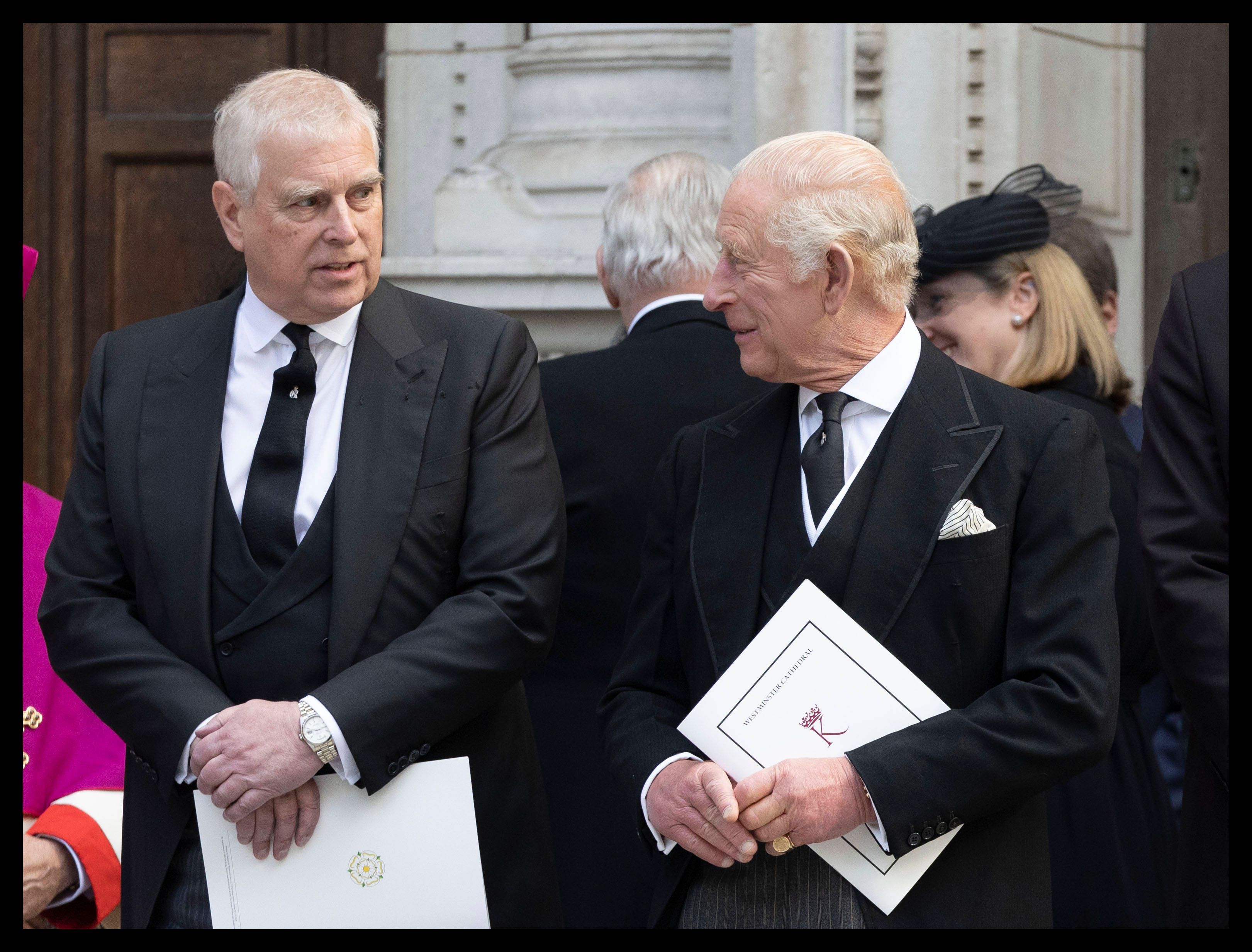 Prinz Andrew und König Charles III unterhalten sich in schwarzen Anzügen und halten Dokumente.