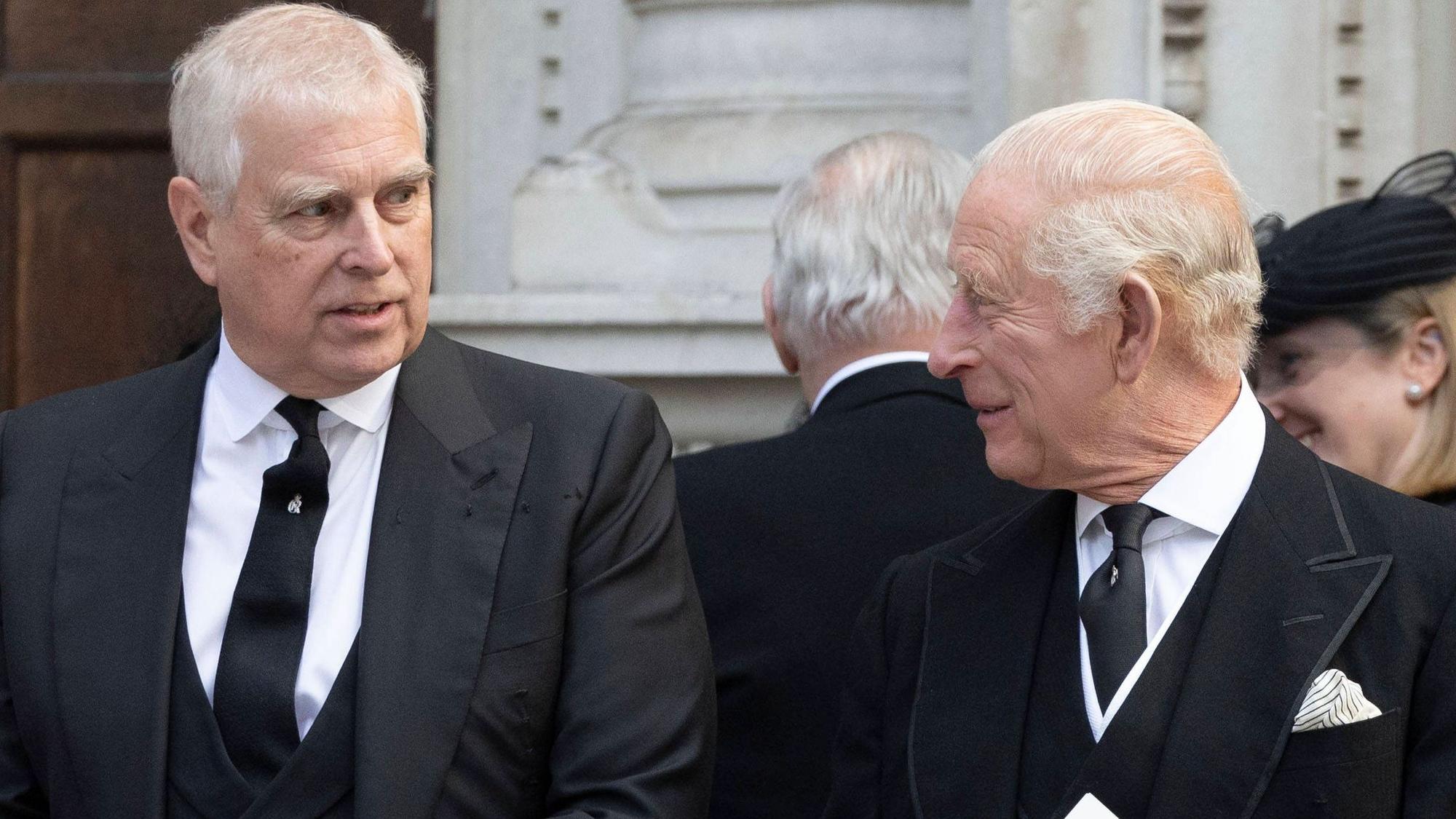 Prinz Andrew und König Charles III unterhalten sich in schwarzen Anzügen und halten Dokumente.