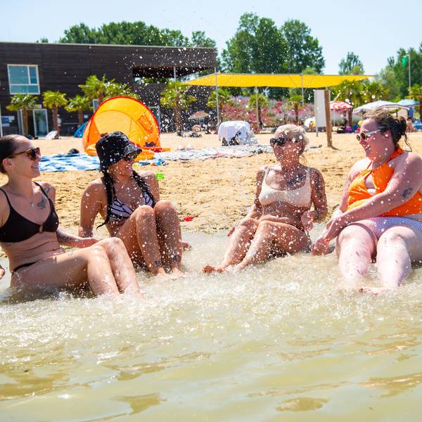 Vier Frauen sitzen im seichten Wasser und spritzen einander nass.