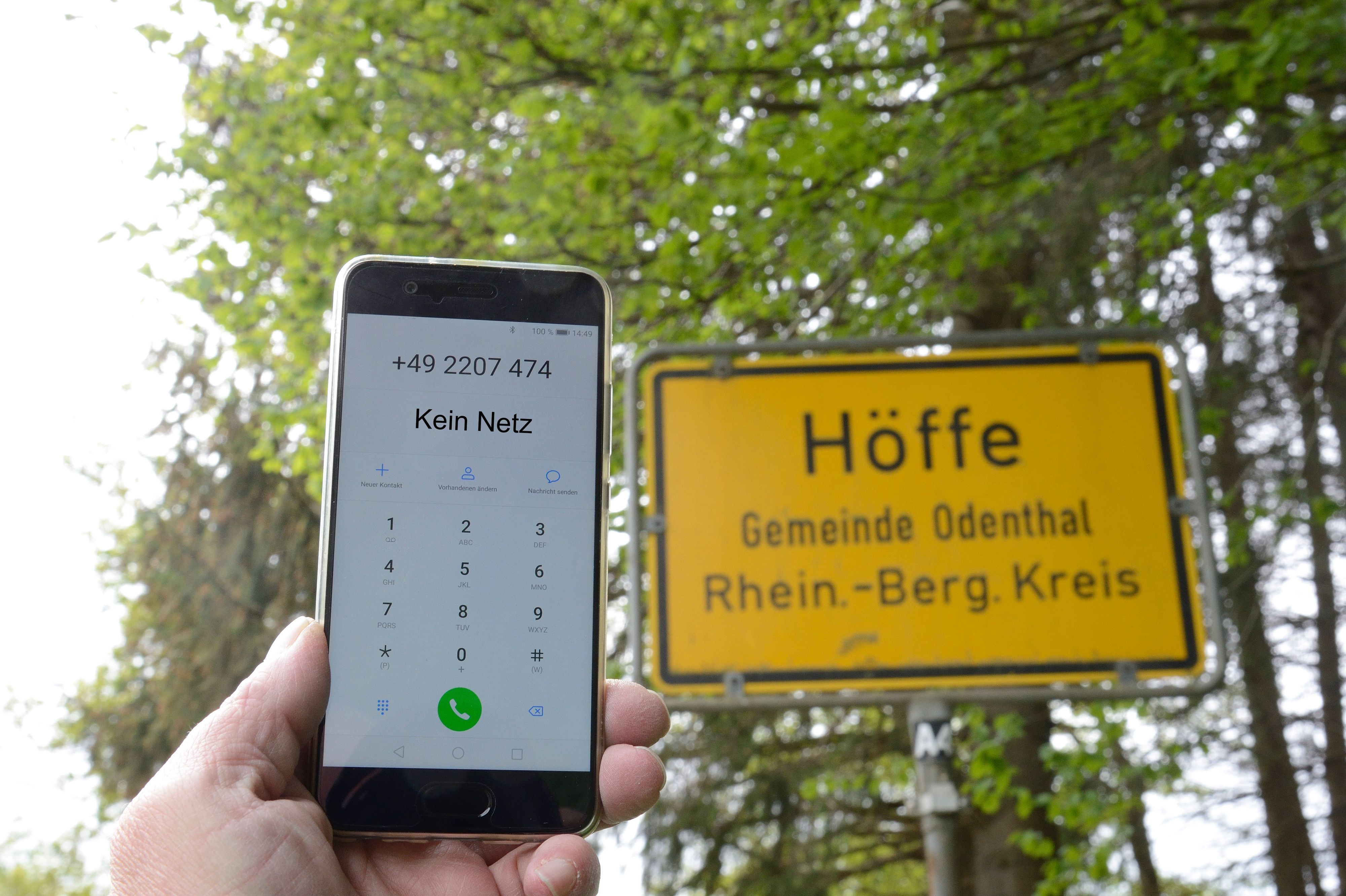 Jemand Halt ein Handy, das kein Netz hat, vor ein Ortschild in Odenthal.