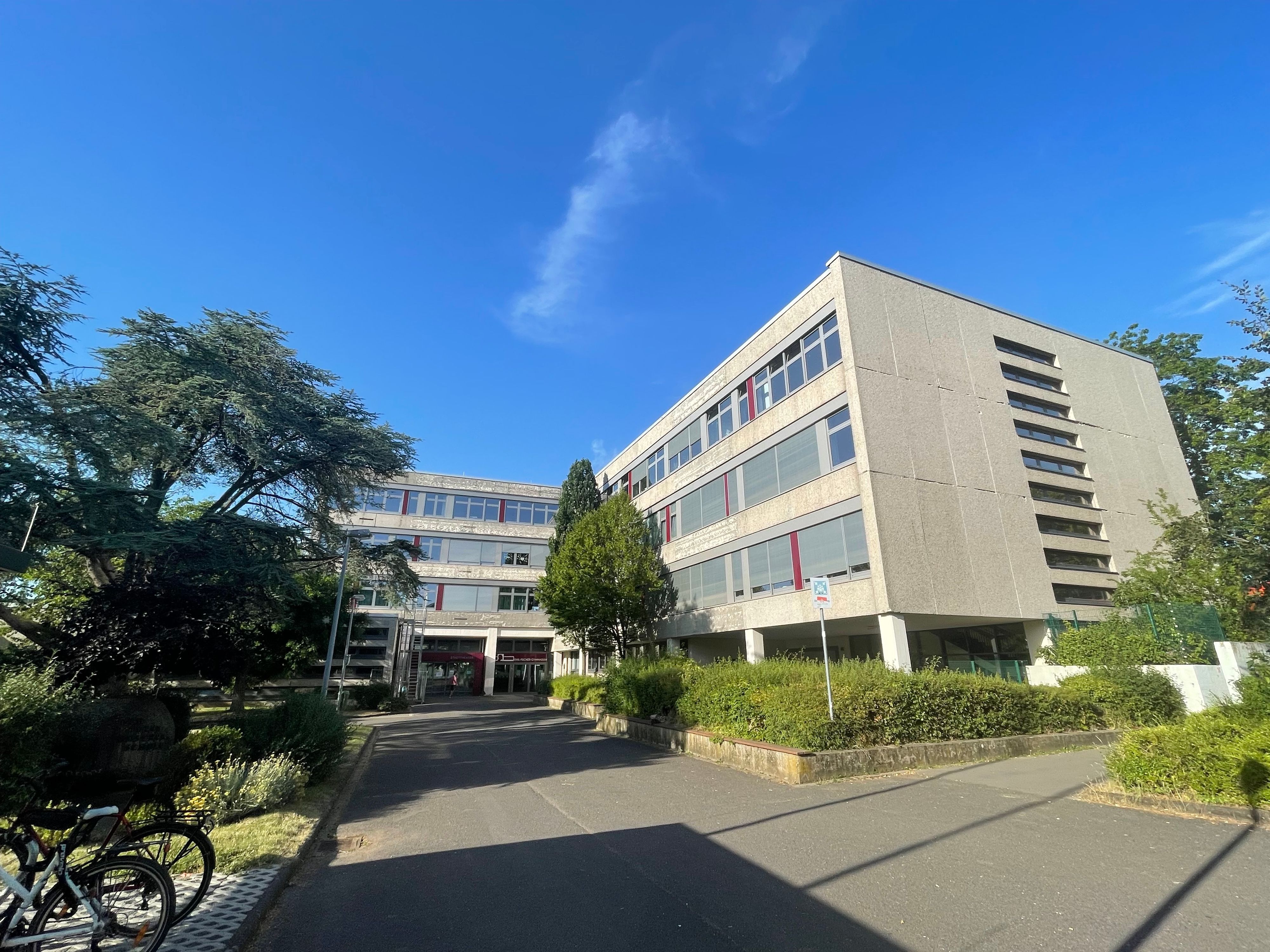 Blick auf das Schulgebäude, das von mehreren Bäumen flankiert wird.