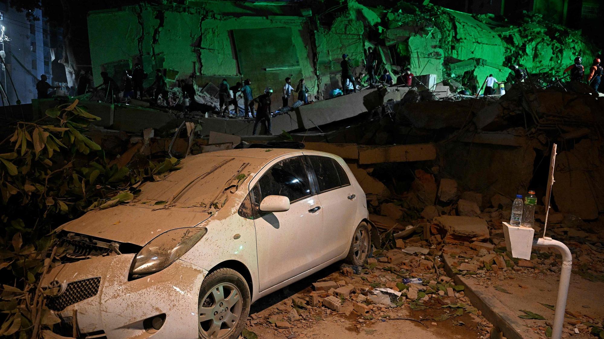Ein von einem umgestürzten Baum zerstörtes Auto ist zu sehen, während Menschen nach dem Erdbeben in Caracas vor einem zerstörten Gebäude vorbeigehen.