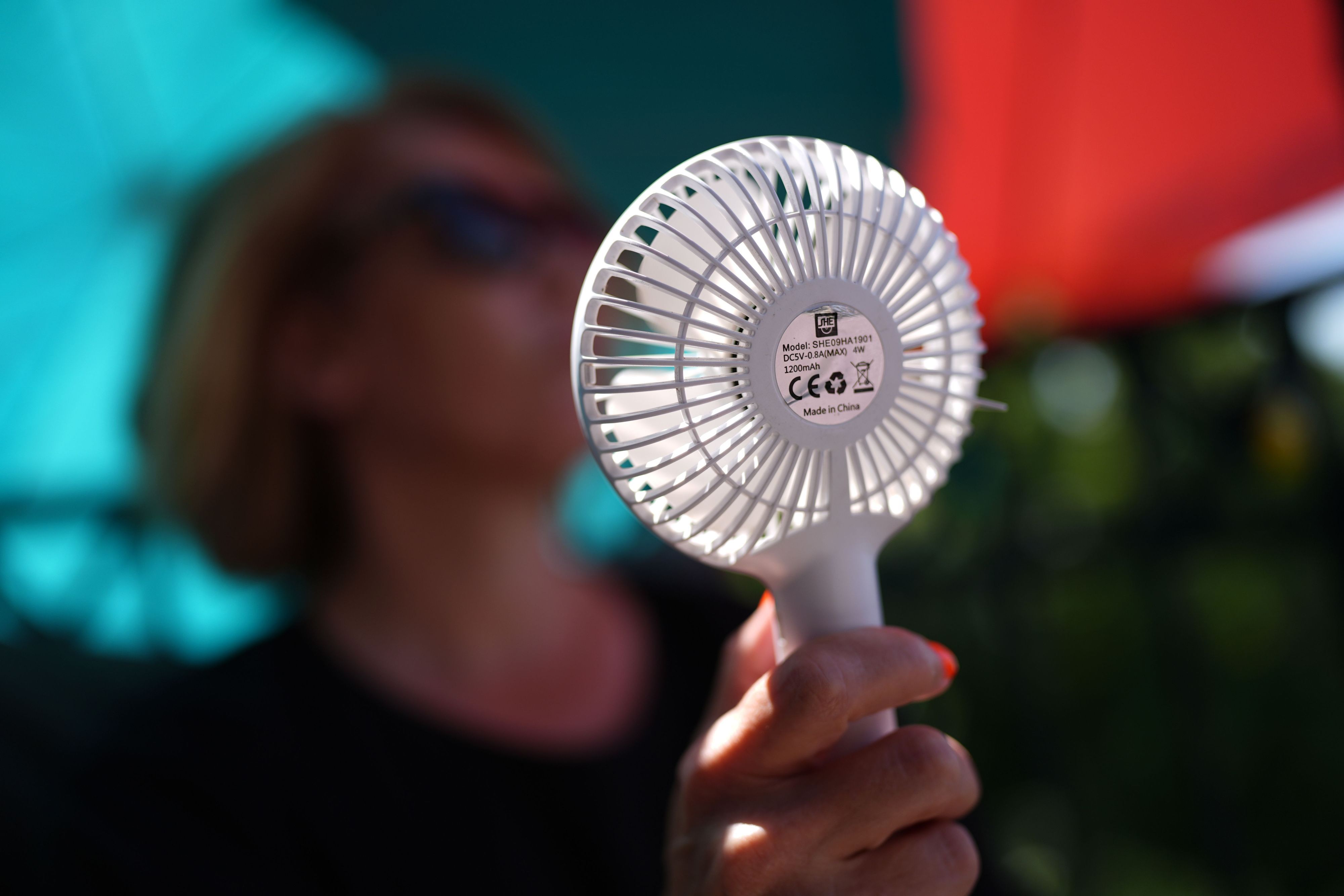 Eine Frau kühlt sich mit einem Handventilator unter Sonnenschirmen auf einem Balkon in der Mittagssonne ab. Die Hitzewelle in Deutschland sorgt aber auch nachts für schweißtreibende Temperaturen. (Symbolbild)