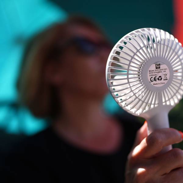 Eine Frau kühlt sich mit einem Handventilator unter Sonnenschirmen auf einem Balkon in der Mittagssonne ab. Die Hitzewelle in Deutschland sorgt aber auch nachts für schweißtreibende Temperaturen. (Symbolbild)