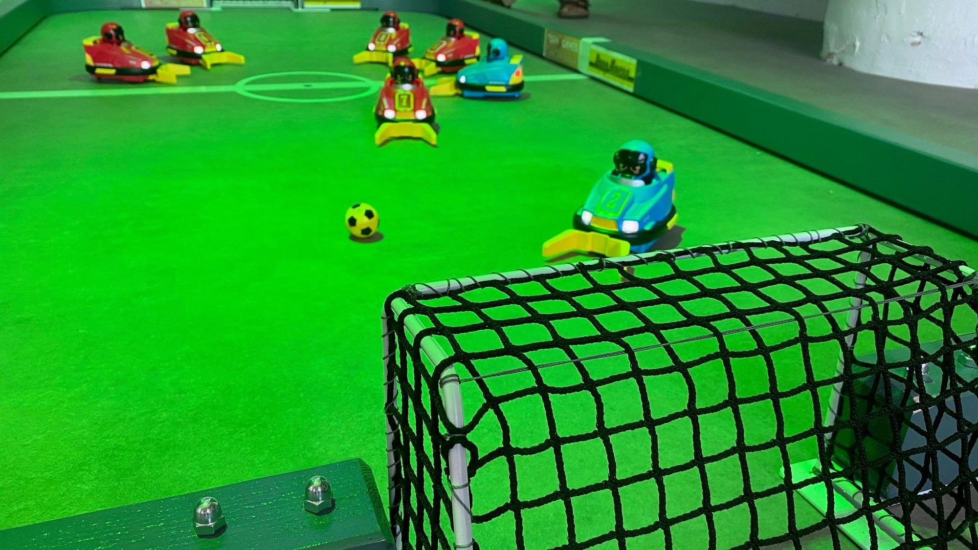 Zu sehen ist ein Miniatur-Fußballfeld mit ferngesteuerten Autos.