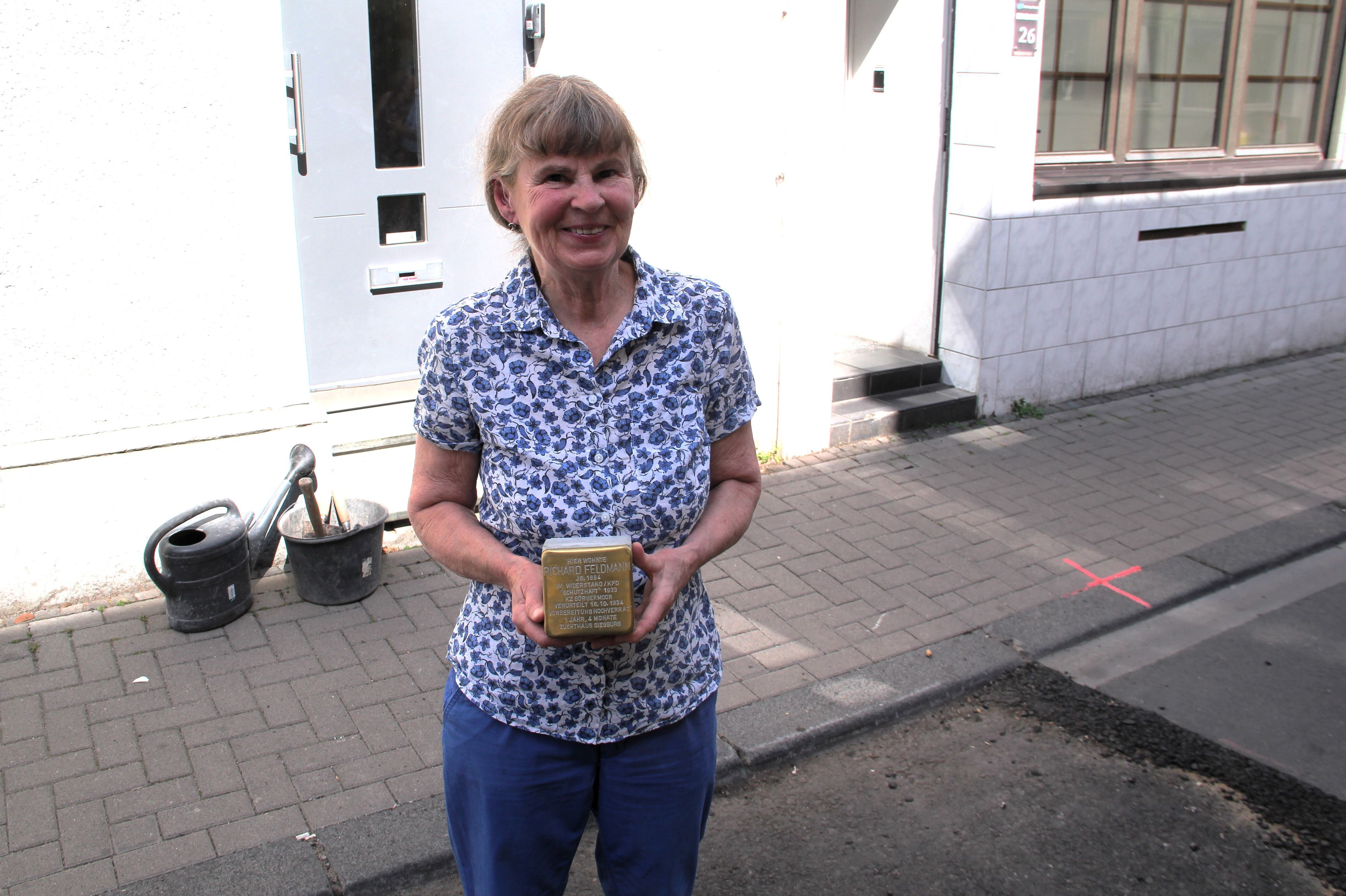 Eine Frau im geblümten Hemd hält einen Stolperstein in den Händen.