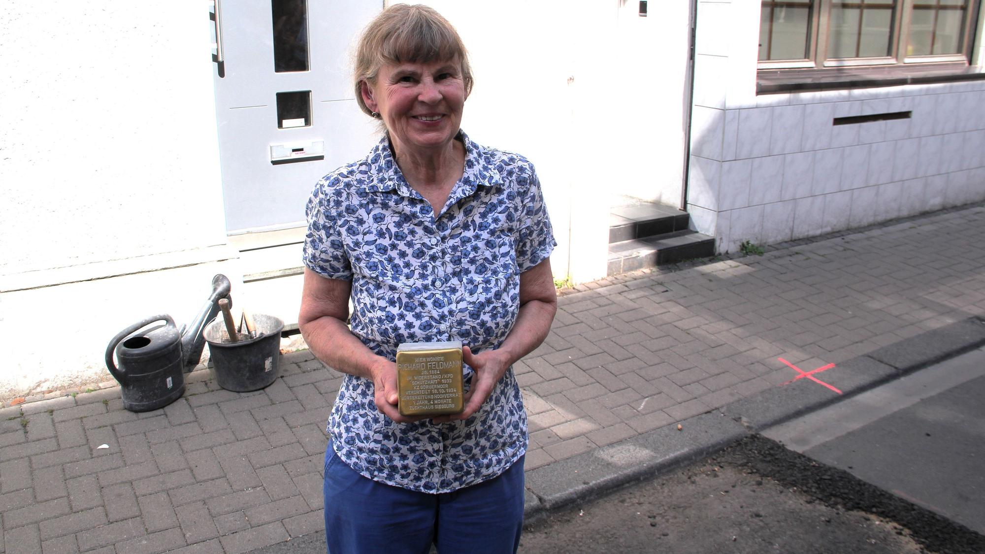 Eine Frau im geblümten Hemd hält einen Stolperstein in den Händen.