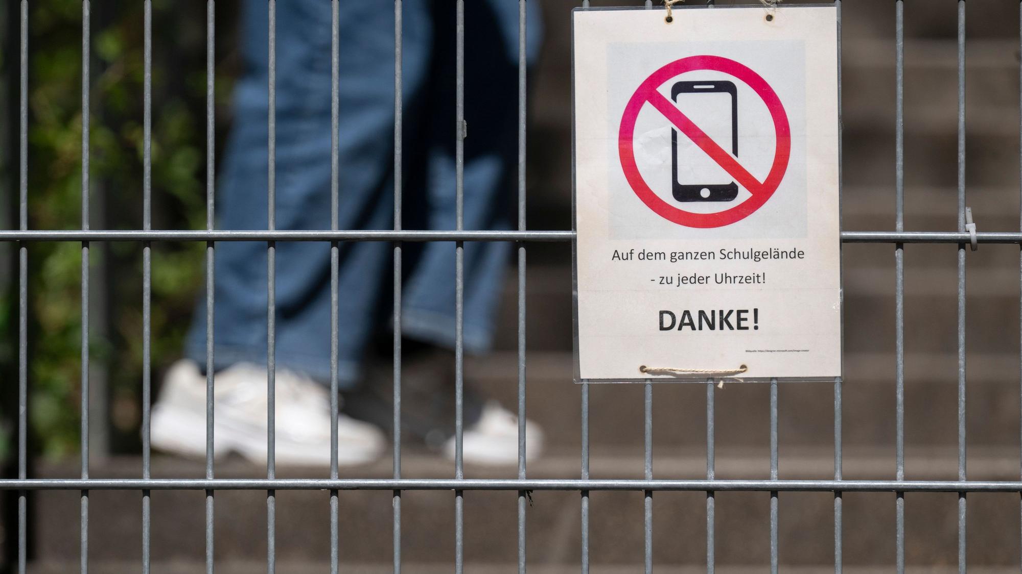 Ein Schild mit einem durchgestrichenen Smartphone und der Aufschrift „Auf dem ganzen Schulgelände – zu jeder Uhrzeit! DANKE!“ hängt am Zugangstor zum Schulhof eines Gymnasiums und weist auf ein generelles Handyverbot hin. Auch dazu hat Karin Prien konkrete Forderungen. (Archivbild)