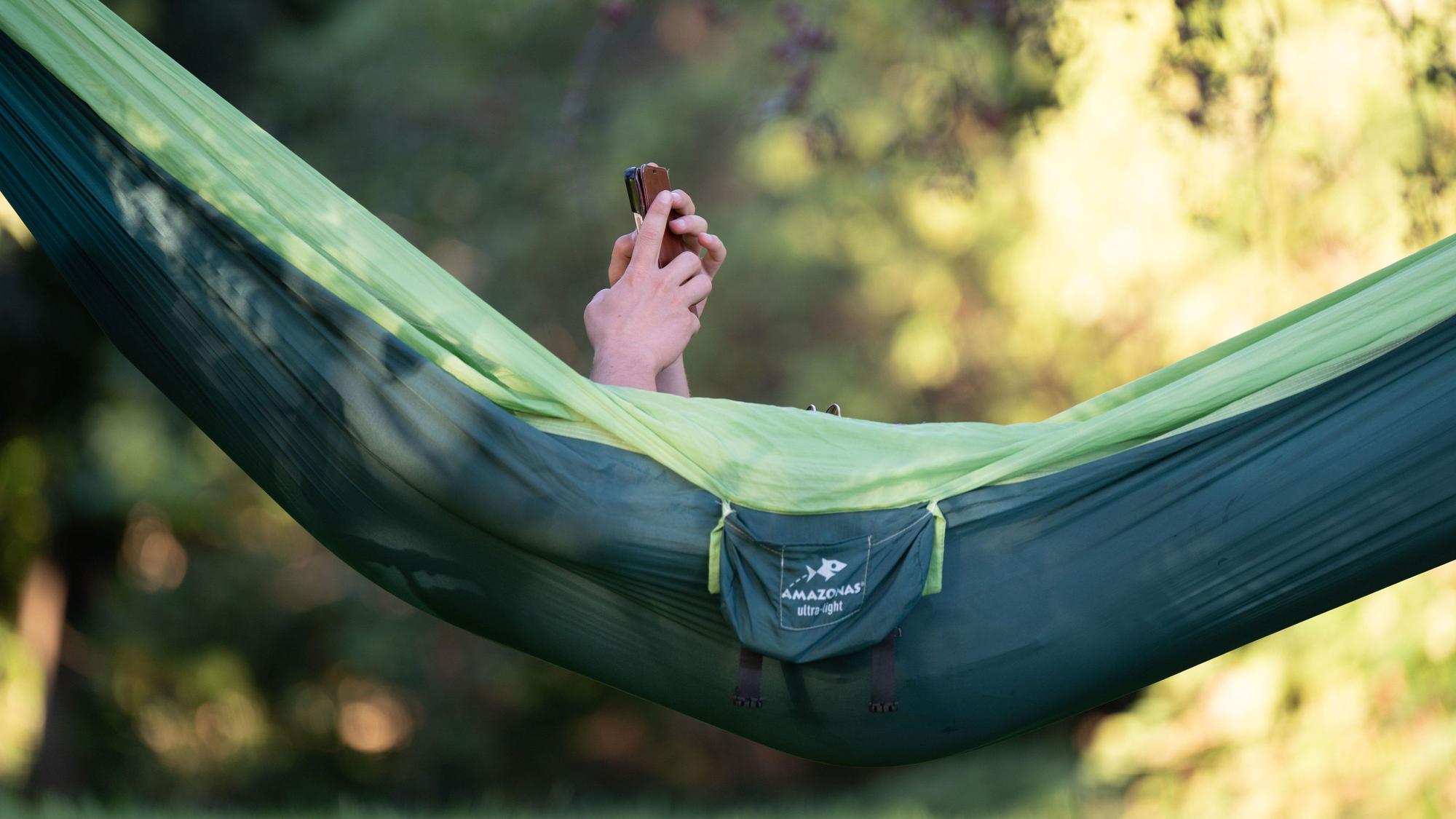 Eine Person liegt draußen in einer Hängematte und schaut auf ihr Smartphone.