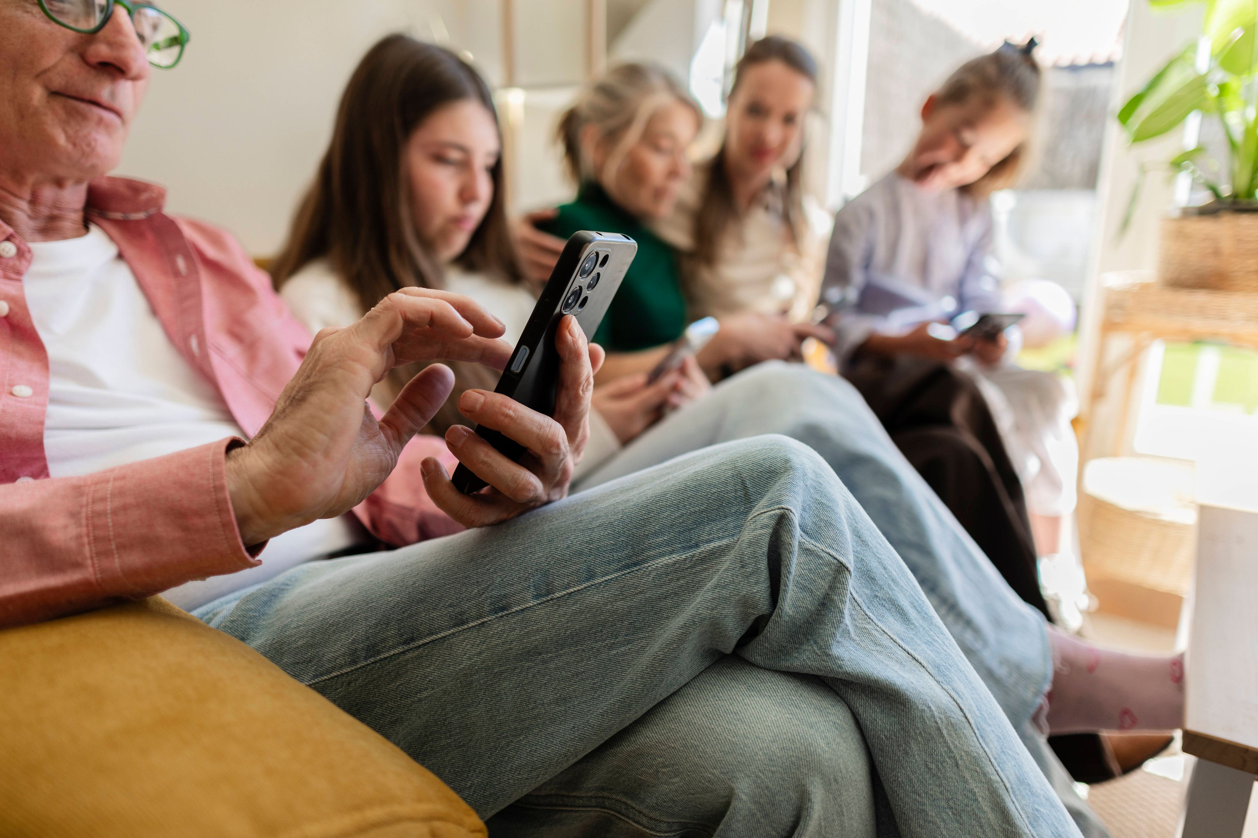 Eine Familie bestehend aus mehreren Generationen sitzt auf einem Sofa und jede Person schaut auf ihr Smartphone.