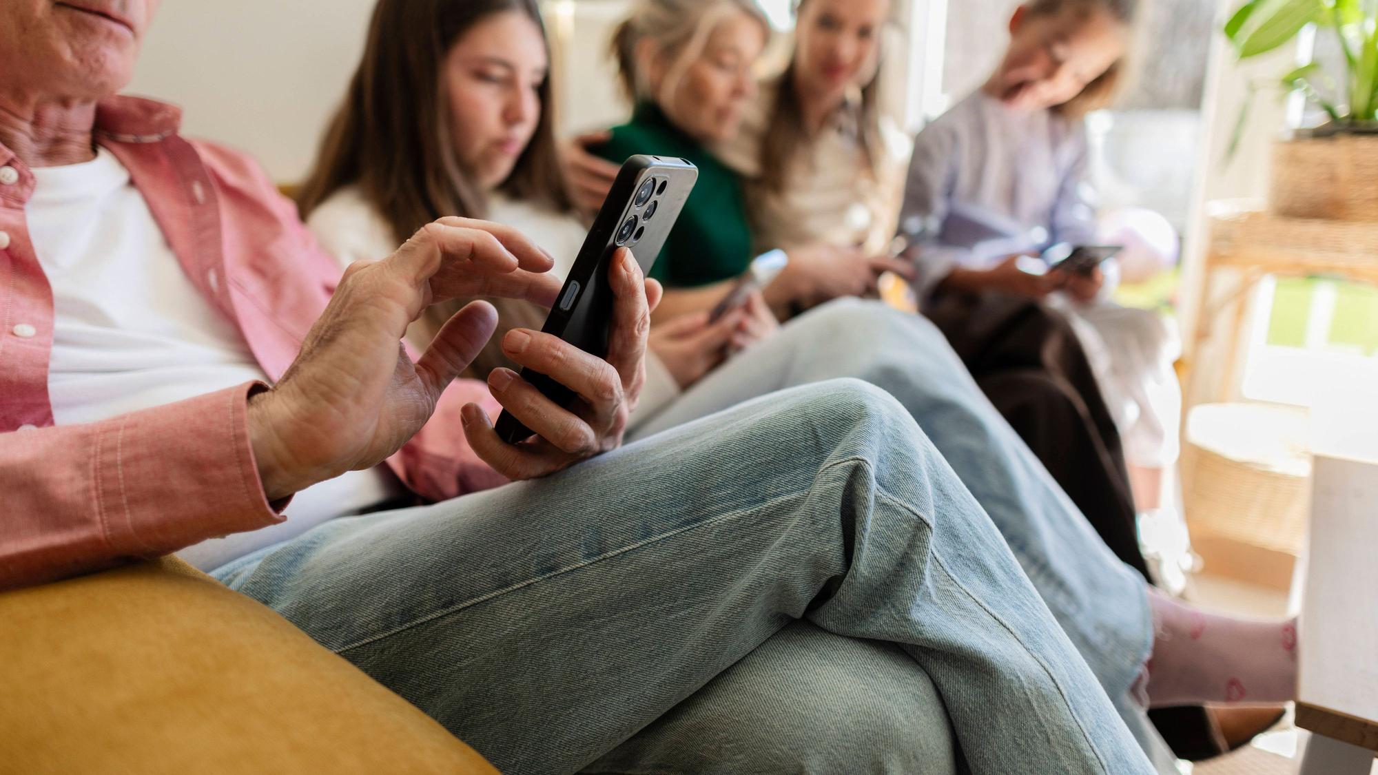 Eine Familie bestehend aus mehreren Generationen sitzt auf einem Sofa und jede Person schaut auf ihr Smartphone.