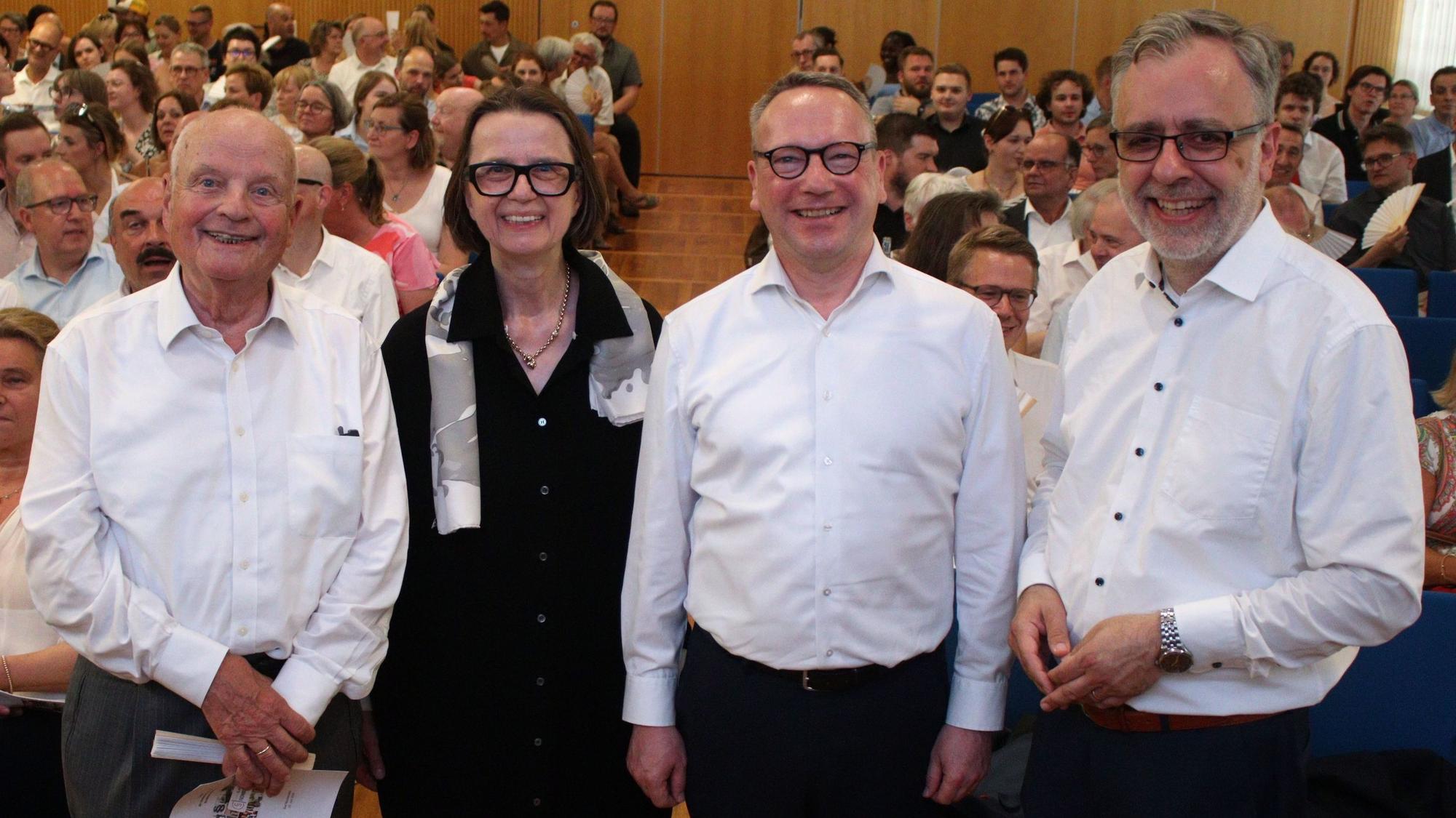 Drei Männer und eine Frau stehen nebeneinander und lachen in die Kamera.