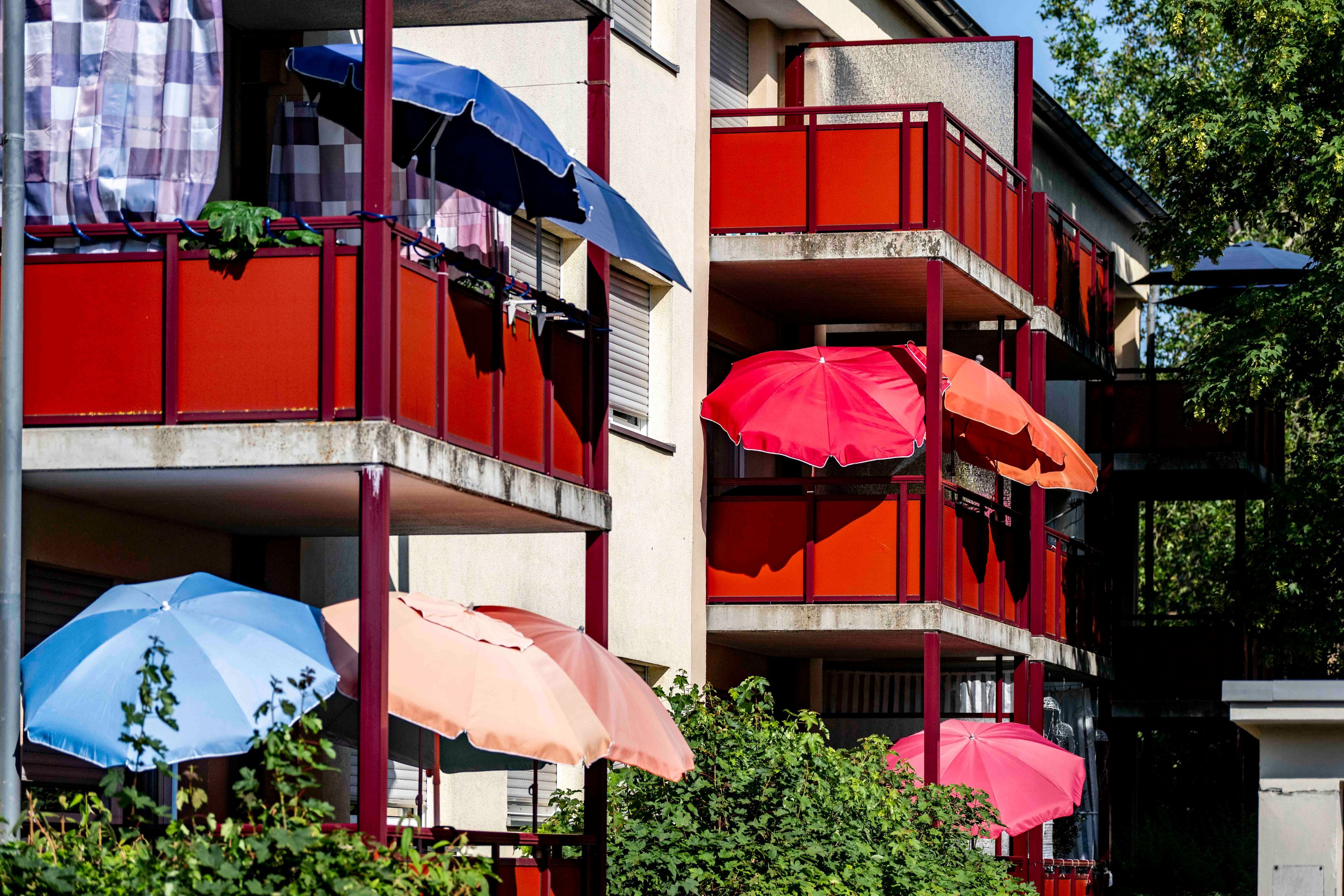 Das Bild zeigt zahlreiche Sonnenschirme, die auf Balkonen an einem Mehrfamilienhaus geöffnet worden sind.