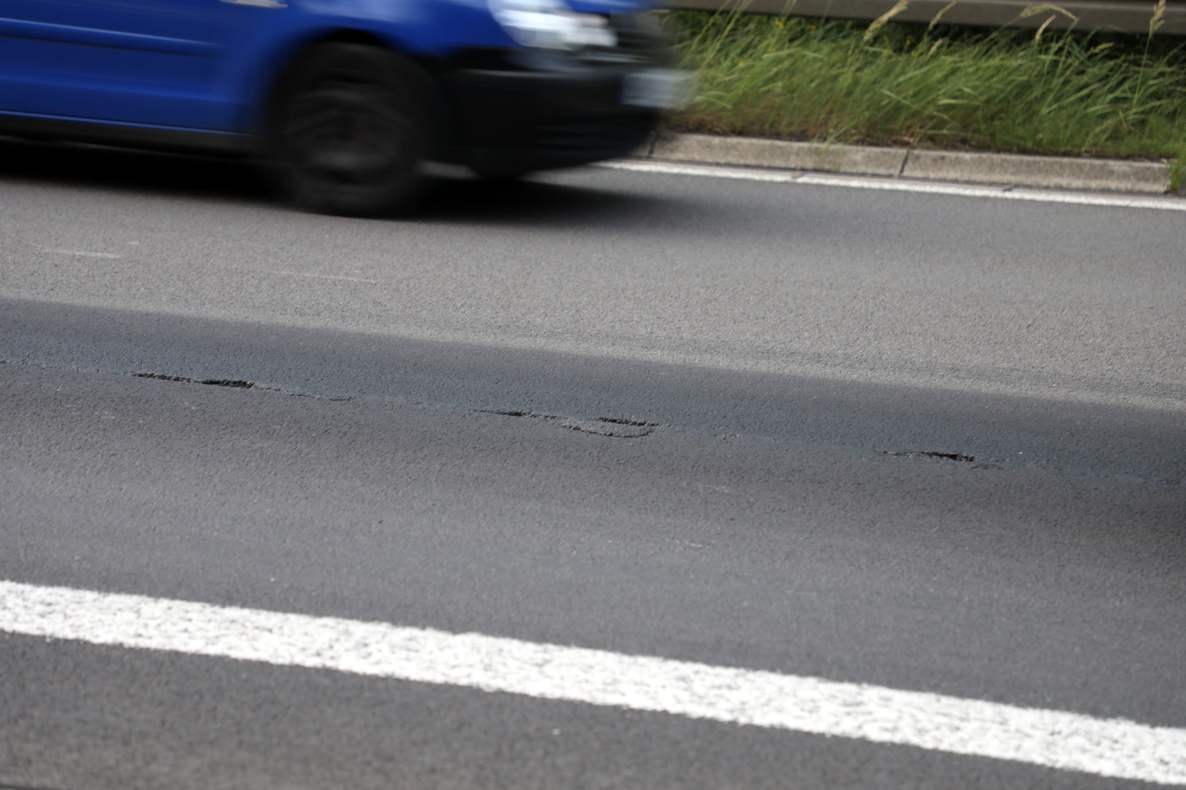 Eine Asphaltfahrbahn reißt auf, im Hintergrund fährt ein Auto vorbei.