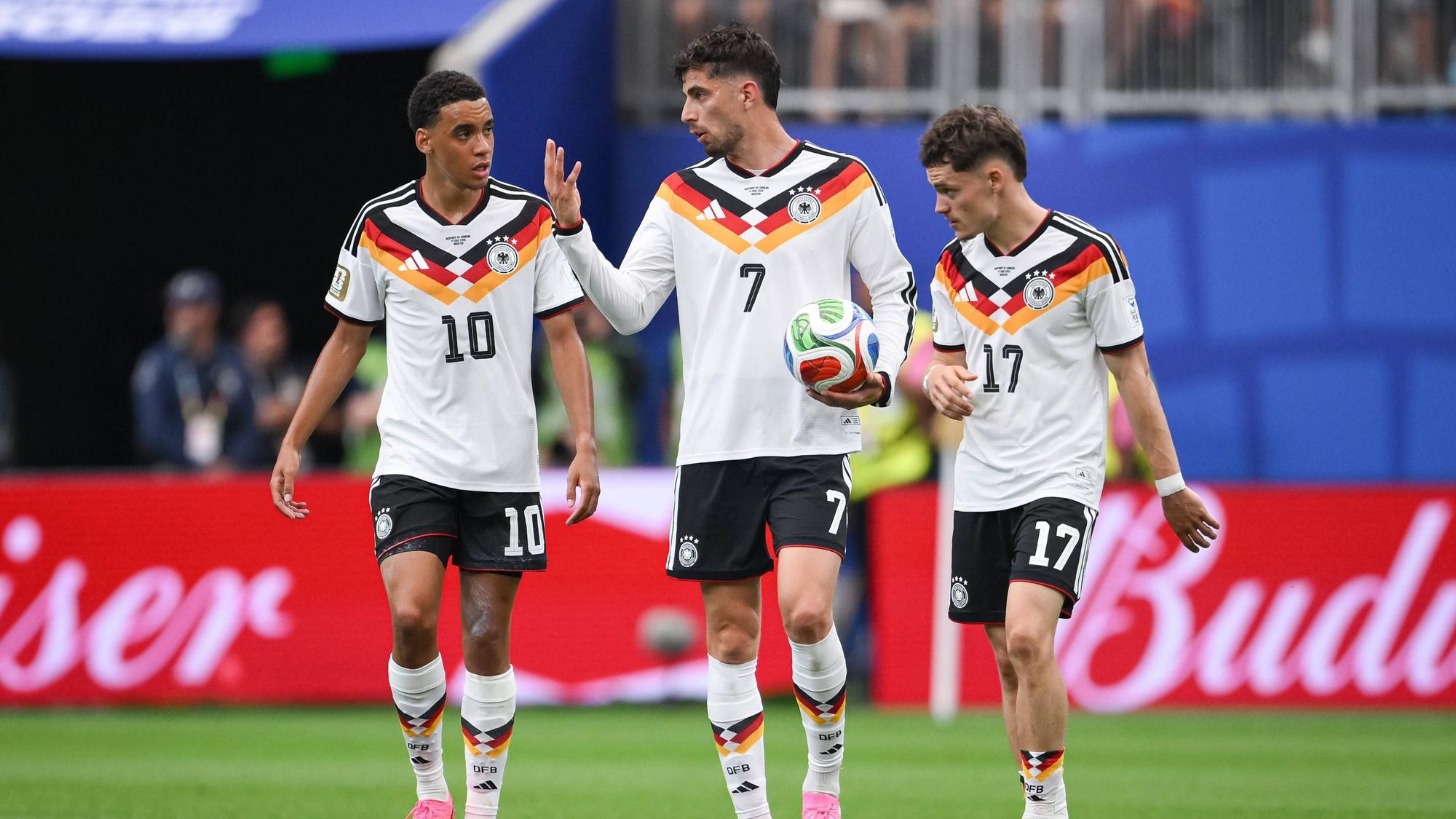 Jamal Musiala, Kai Havertz und Florian Wirtz diskutieren nachdenklich im DFB-Trikot.