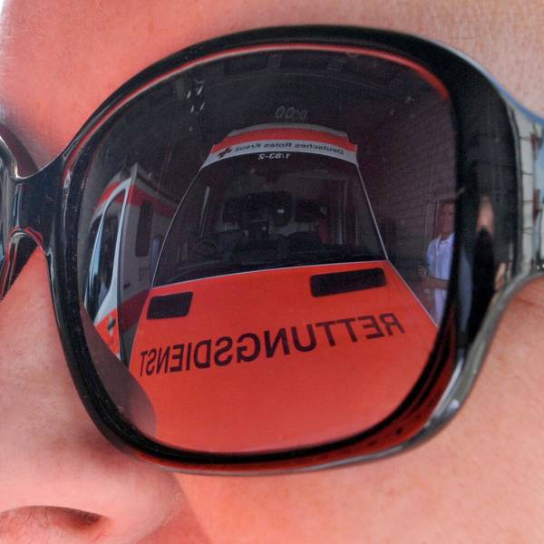 Ein Rettungswagen spiegelt sich in der Sonnenbrille einer Rettungsassistentin.