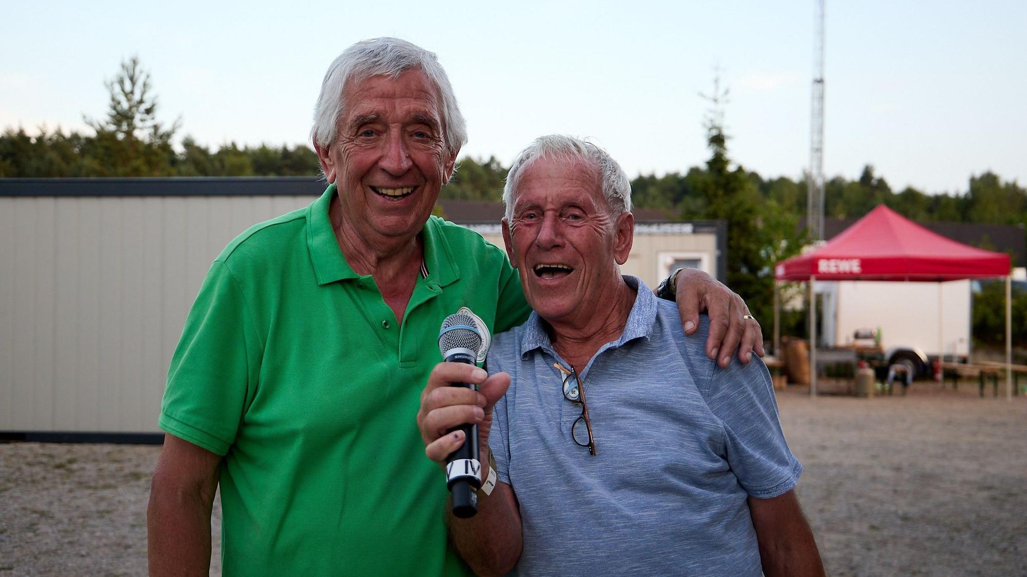 Zwei Männer stehen nebeneinander, einer hält ein Mikrofon.