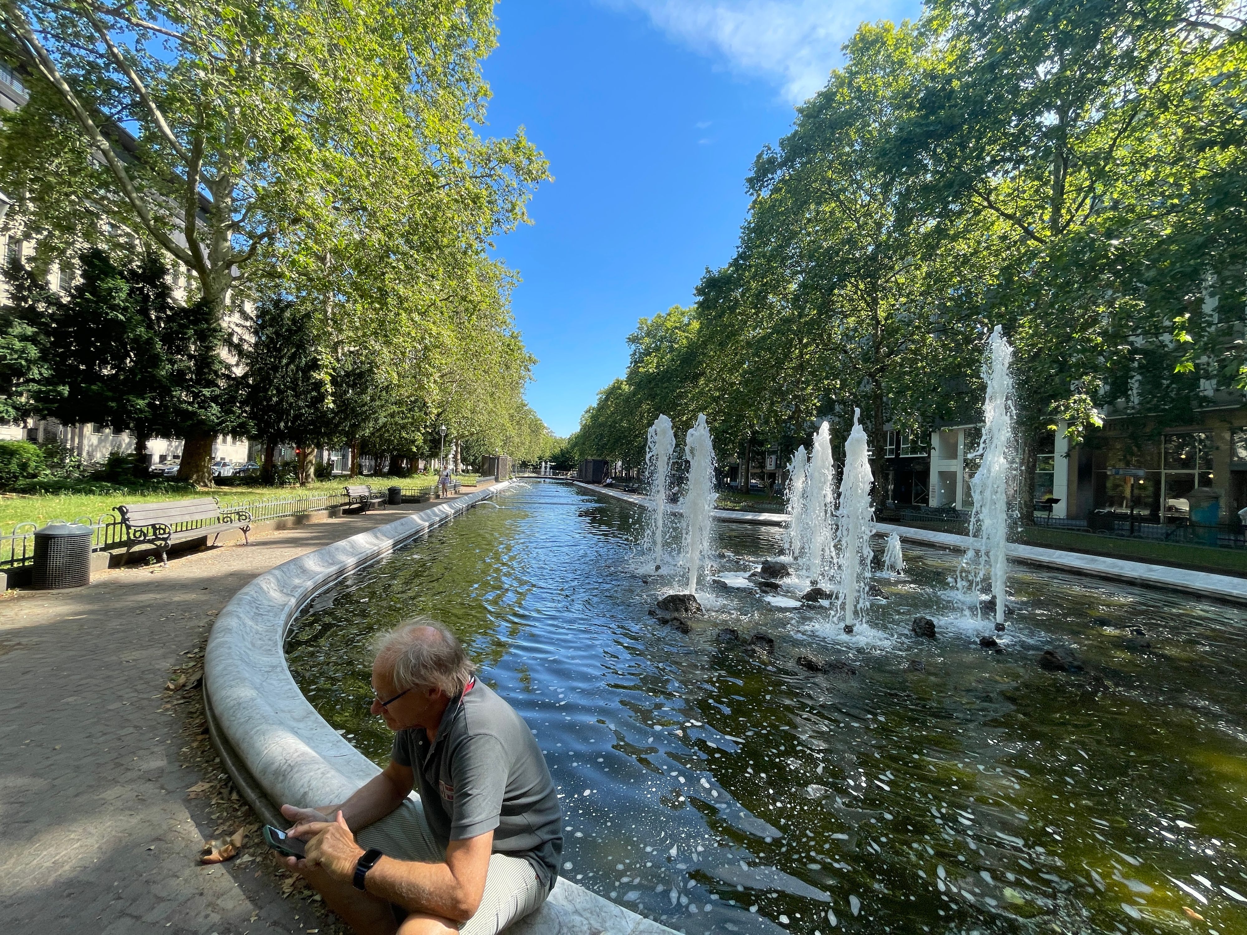 Ein Mann sitzt am Rand des Springbrunnens am Kaiser-Wilhelm-Ring.