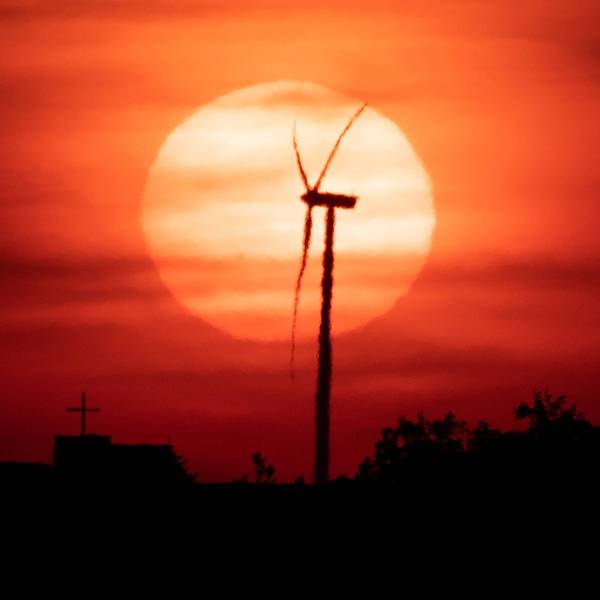 Die Sonne geht vor einem Windrad unter.